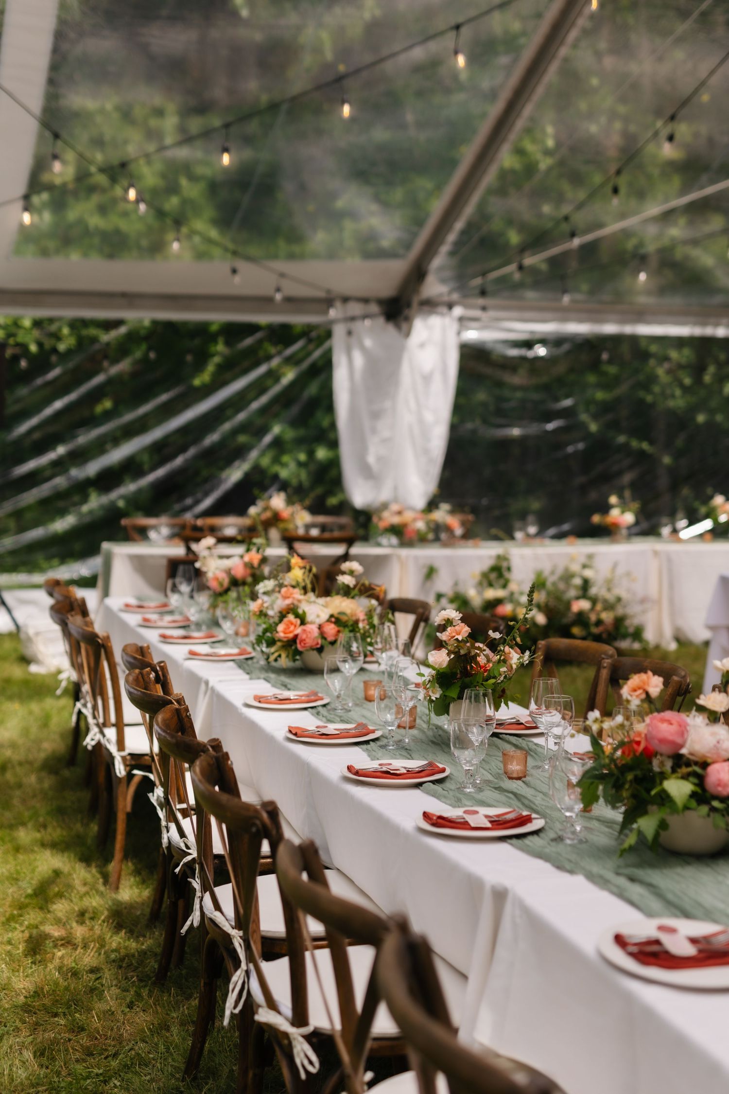 Elegant outdoor wedding reception table set with white linens, rustic chairs, and peach floral centerpieces under string lights.