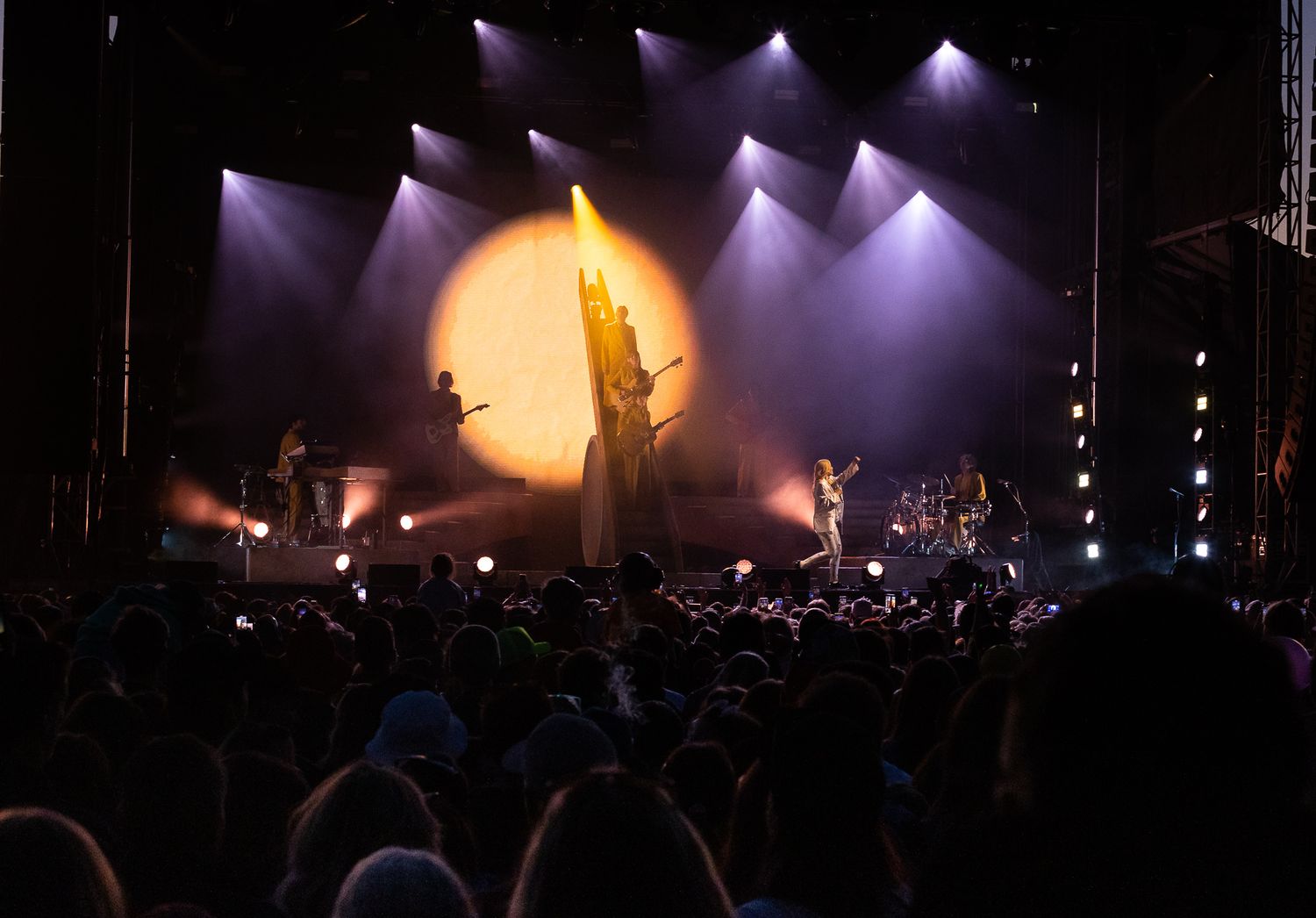 Concert stage with dramatic orange backlight and silhouetted performers in front of crowd.