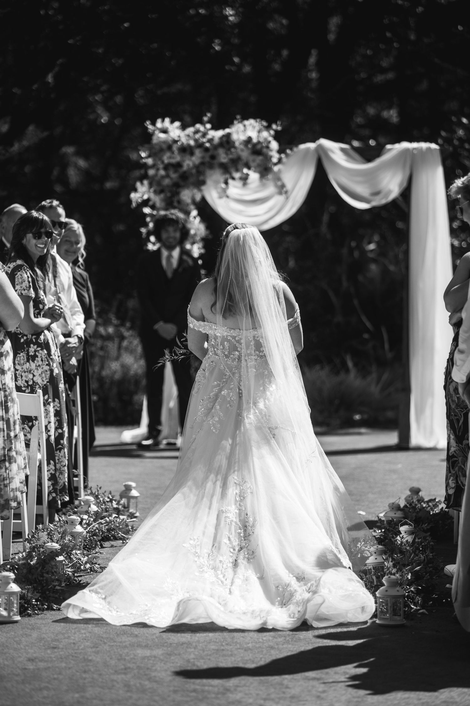 A stunning cathedral-length veil and train flow behind a bride at an outdoor ceremony.