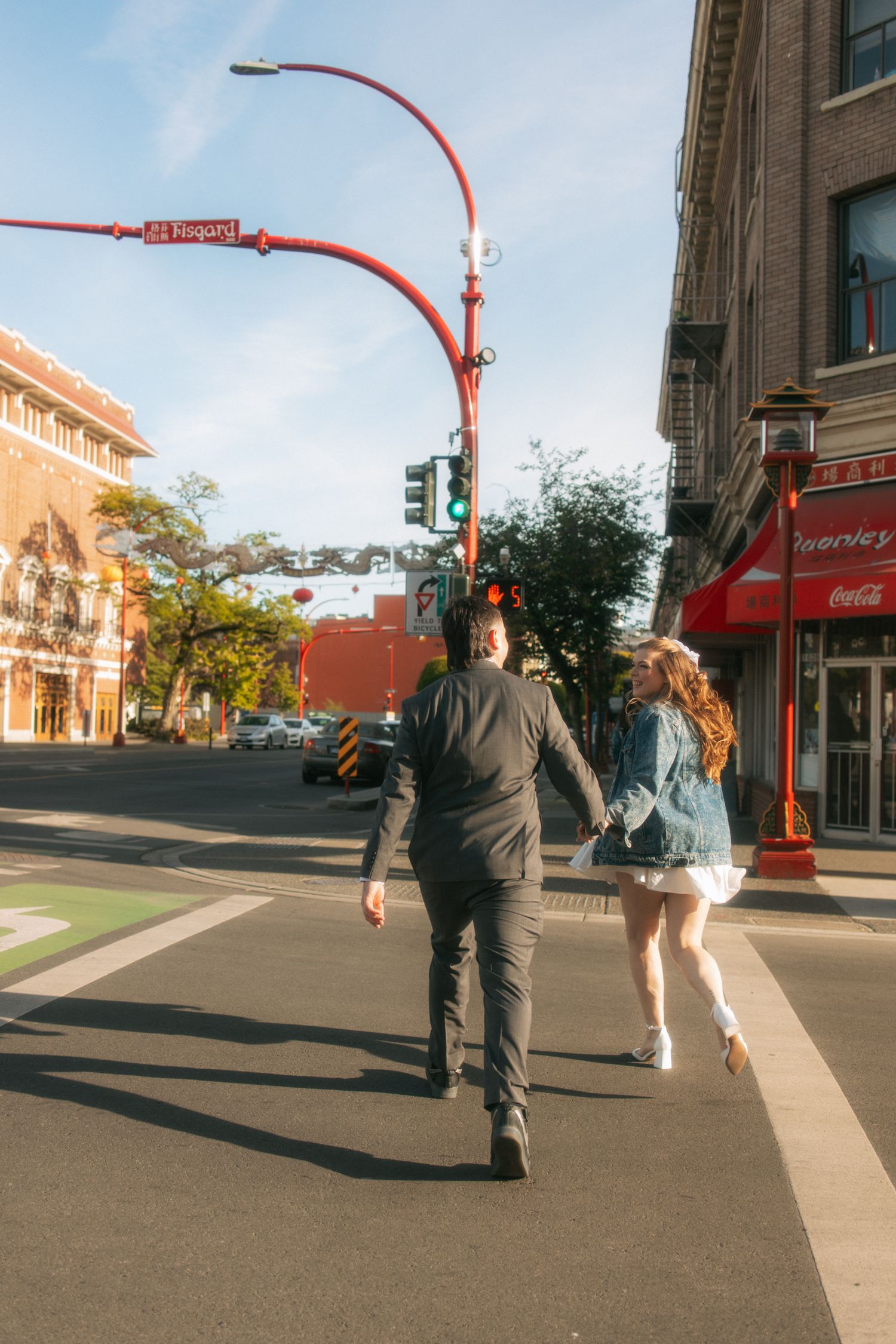 Two people walk down a sunny urban street with distinctive red lamp posts and historic buildings in Edmonton, Alberta.