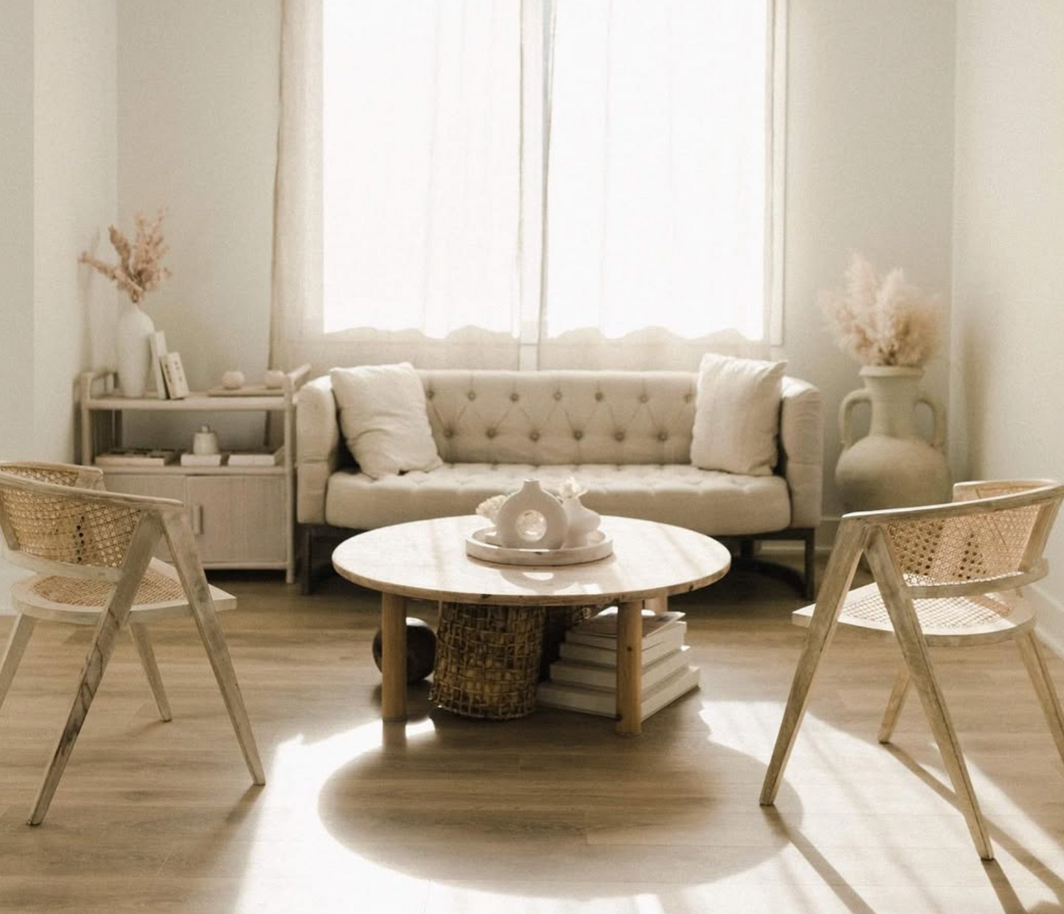 Minimalist living space featuring tufted cream sofa, white round table, and rattan accent chairs.