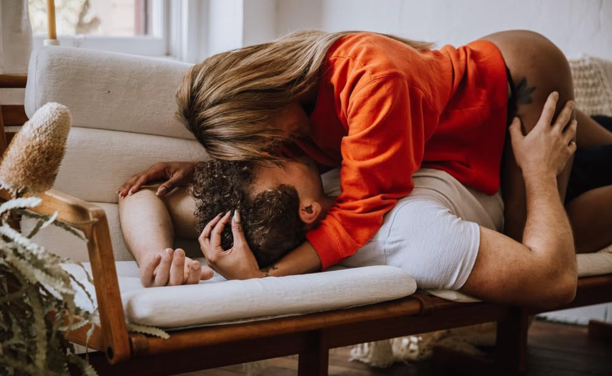 Couple sharing an intimate moment on a white couch in natural light.