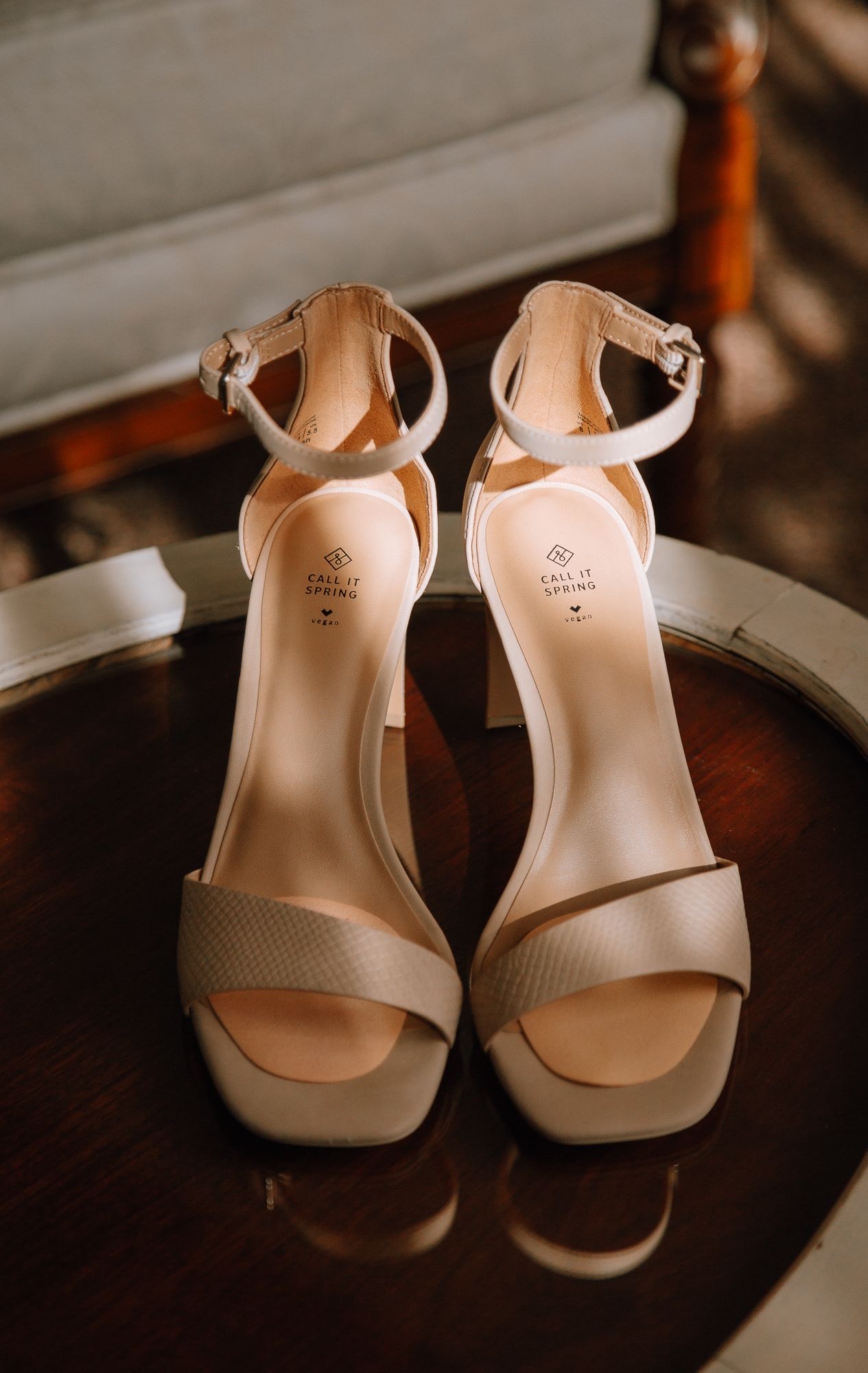 Elegant cream-colored ankle strap sandals with block heels displayed on a dark wooden table.