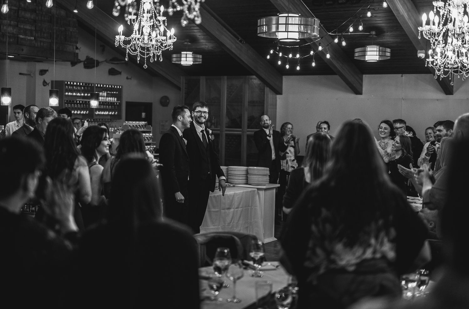 Black and white reception photo with crystal chandeliers and gathered wedding guests.