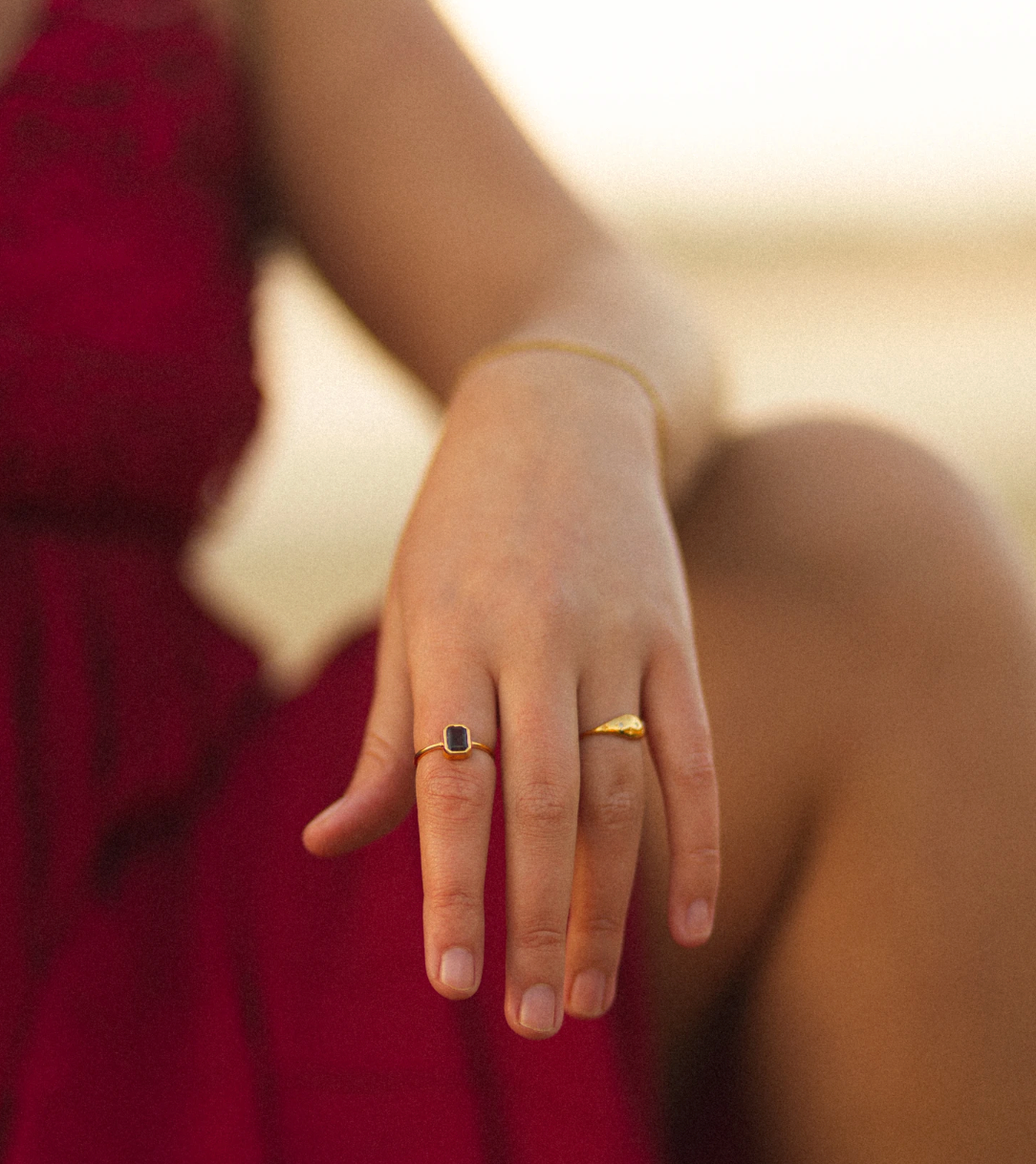 Hand displaying two rings against a burgundy dress in warm sunlight.