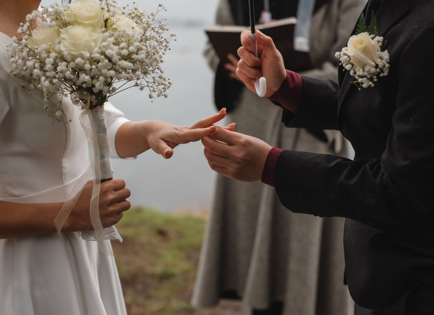 Wedding ceremony moment showing hands exchanging rings with white baby's breath bouquet.