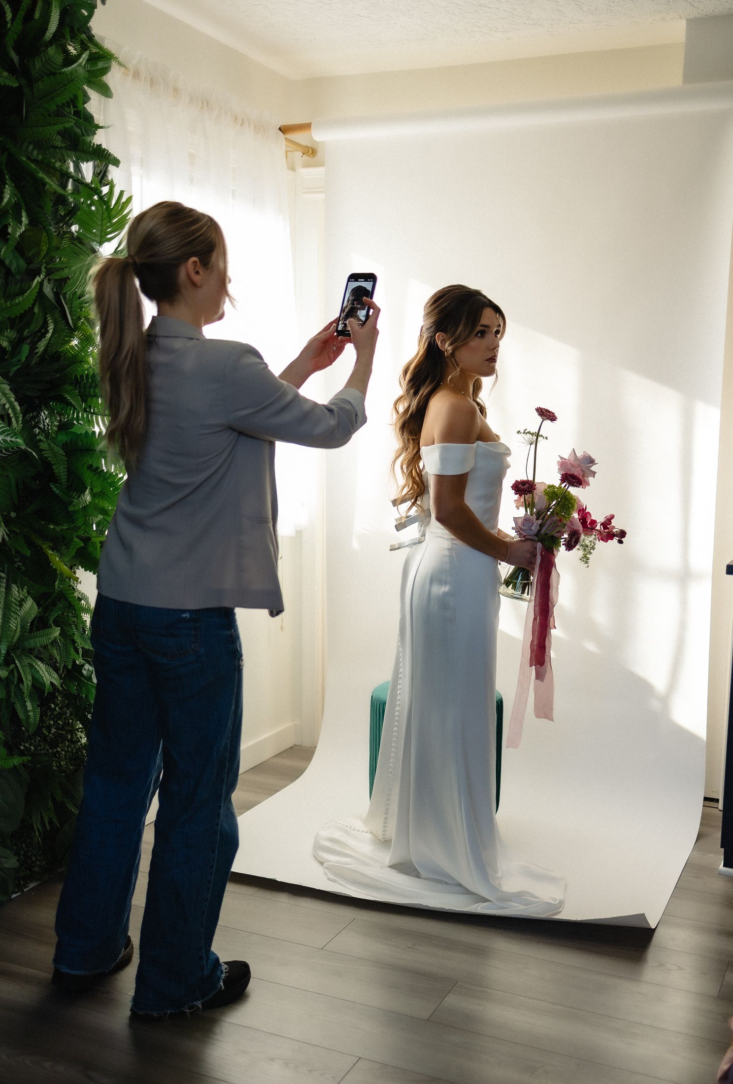 Behind-the-scenes photography session showing a person photographing someone wearing a white dress and holding a floral bouquet.