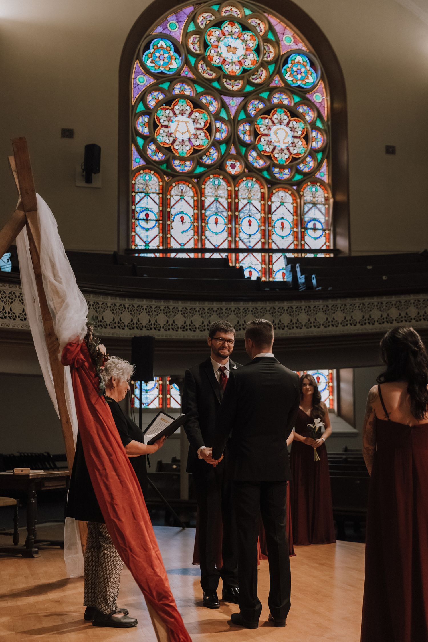 Wedding party gathering in a church beneath ornate stained glass windows and decorative walls.