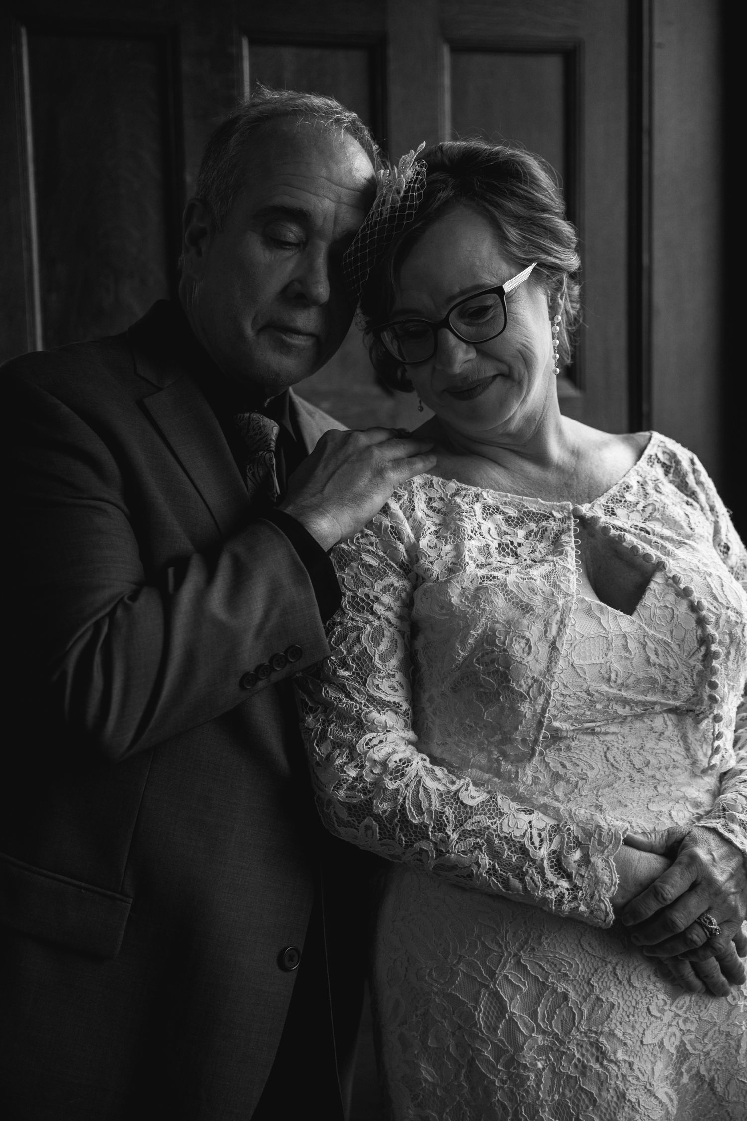 An intimate black and white portrait of a couple in formal wedding attire sharing a tender moment.