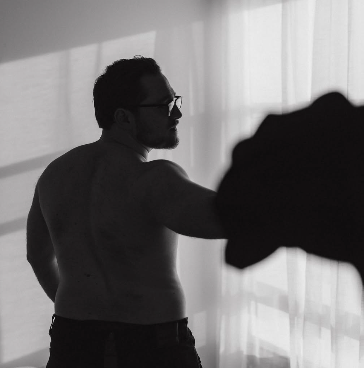 Silhouetted figure in glasses casting shadow on white wall in natural light.