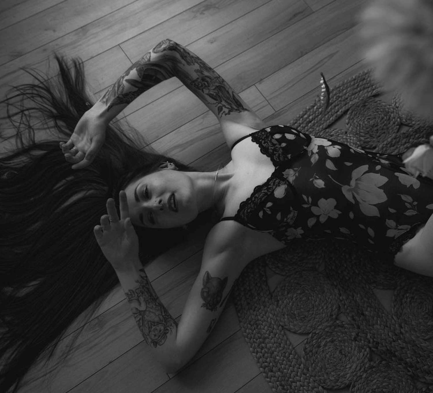 Artistic black and white photo of person laying on wooden floor with long dark hair spread out.