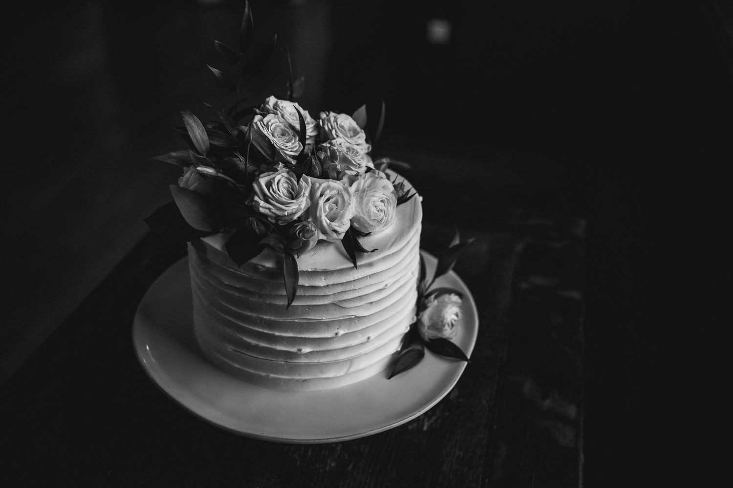 A black and white photo of a textured wedding cake decorated with fresh roses on top.
