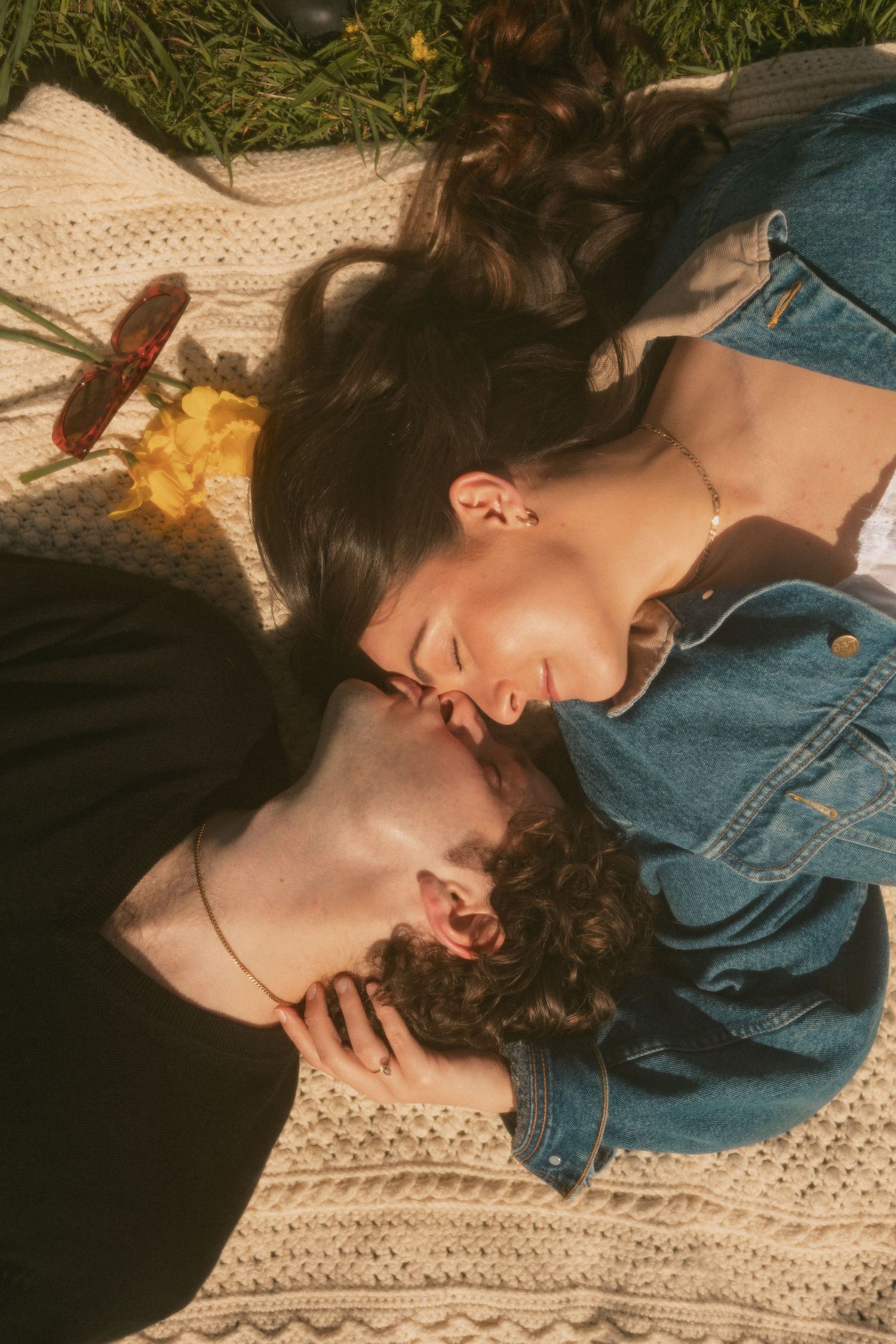 Two people lying on a knit blanket outdoors in denim clothing.