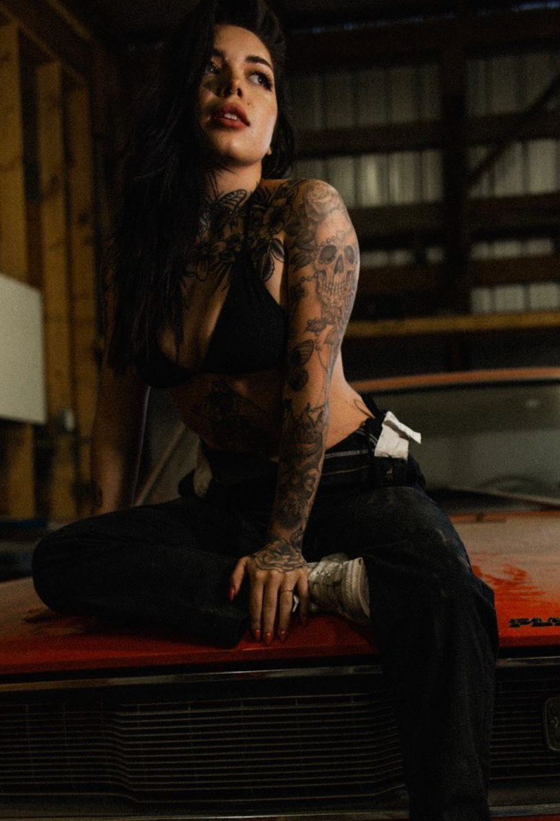 Edgy portrait of tattooed woman in black attire sitting on industrial surface.