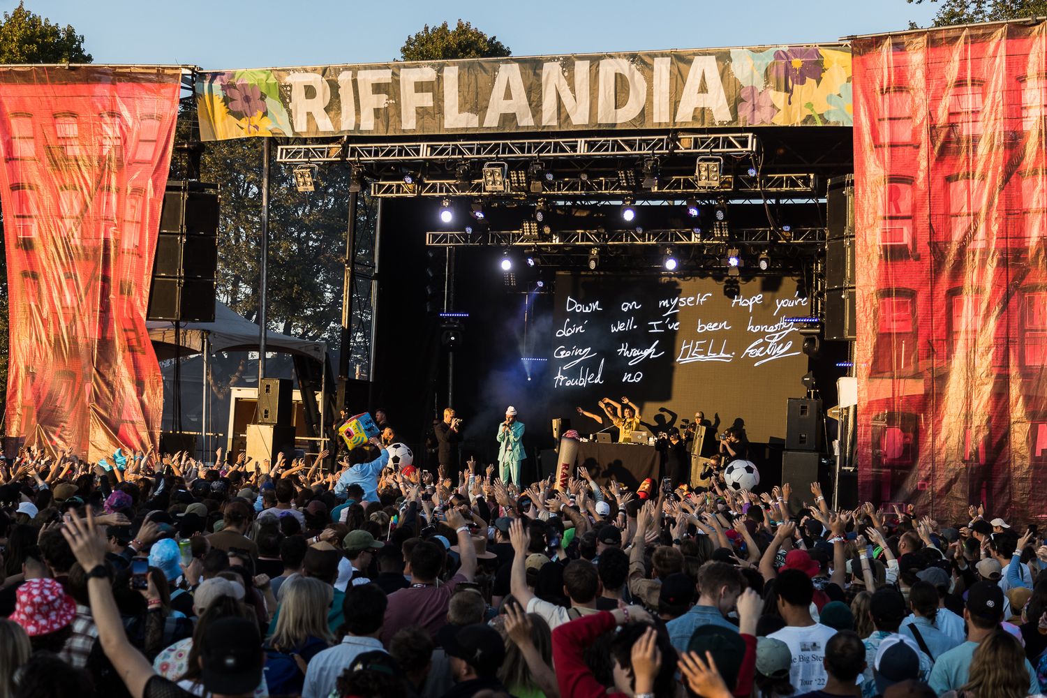 Large crowd watching a performance at Rifflandia music festival with colorful banners and stage setup at sunset.
