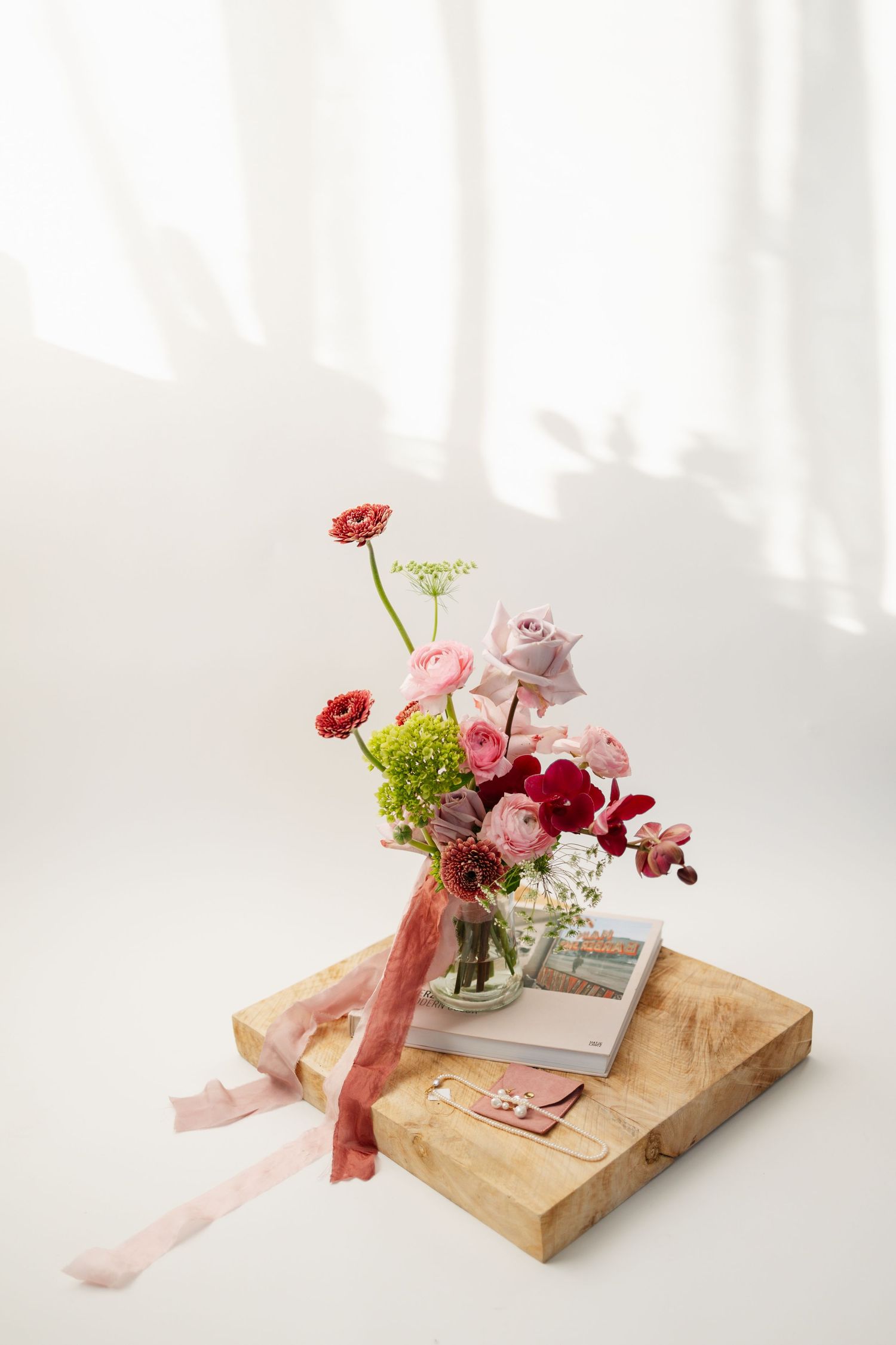 A romantic floral arrangement with pink and red blooms on a wooden tray with ribbons.