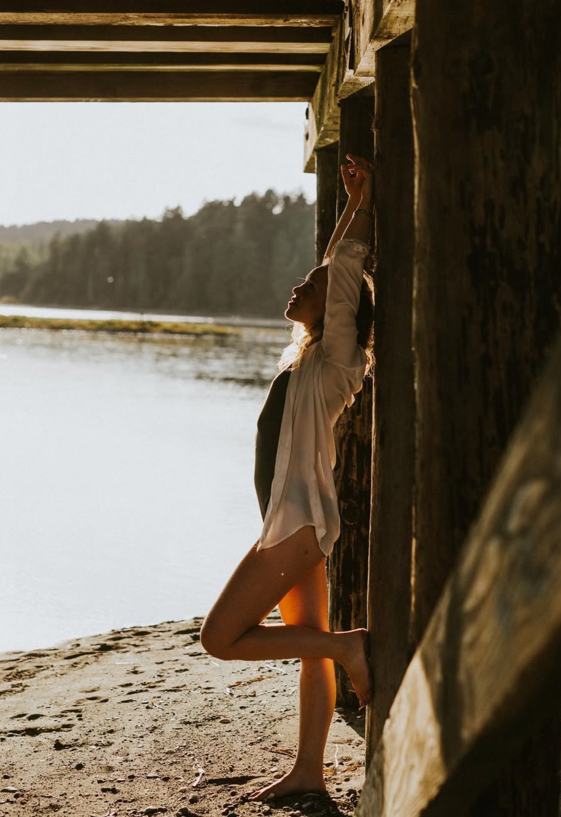 Silhouette against bright waterfront view through rustic wooden structure at sunset.