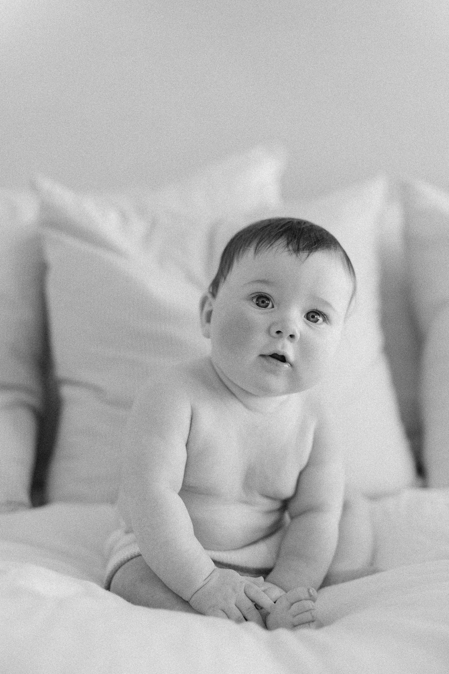 Black and white series of photos showing a baby lying on white bedding peeking at the camera.