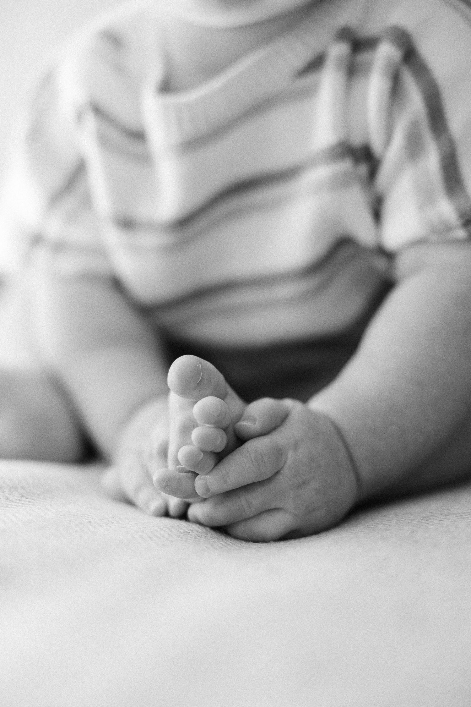 Close-up black and white photo of a baby's tiny feet and hands resting on a soft white surface.