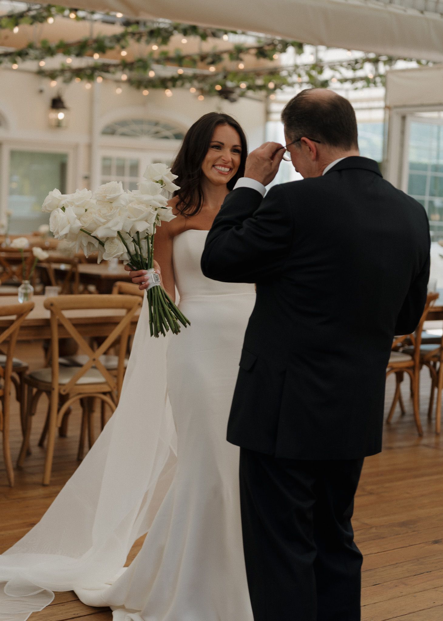 Bride sharing a first look with her father at an elegant Hamptons wedding reception, under string lights and wooden beams.
