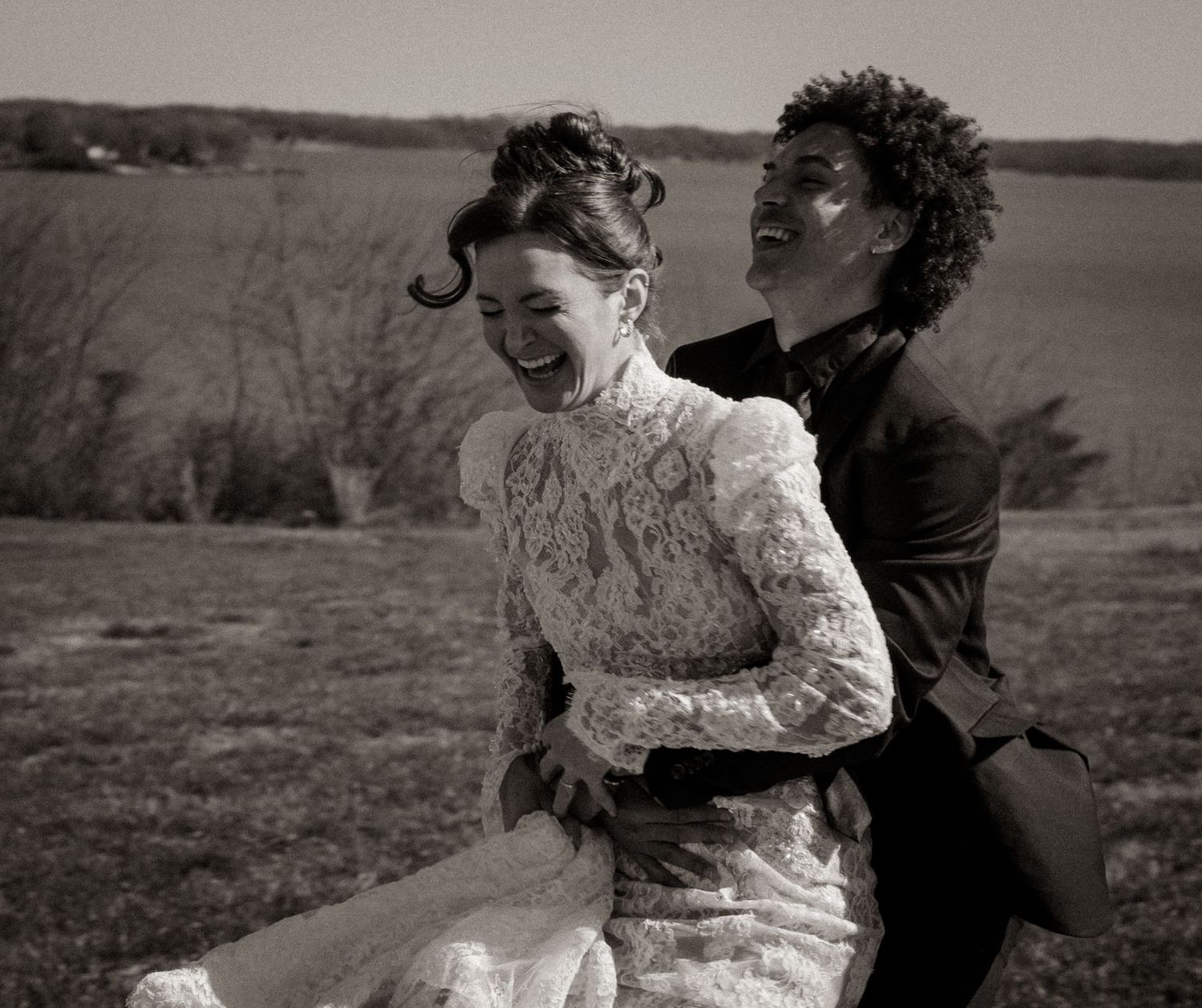 Two people in a candid moment share laughter while embracing in a black and white outdoor portrait.