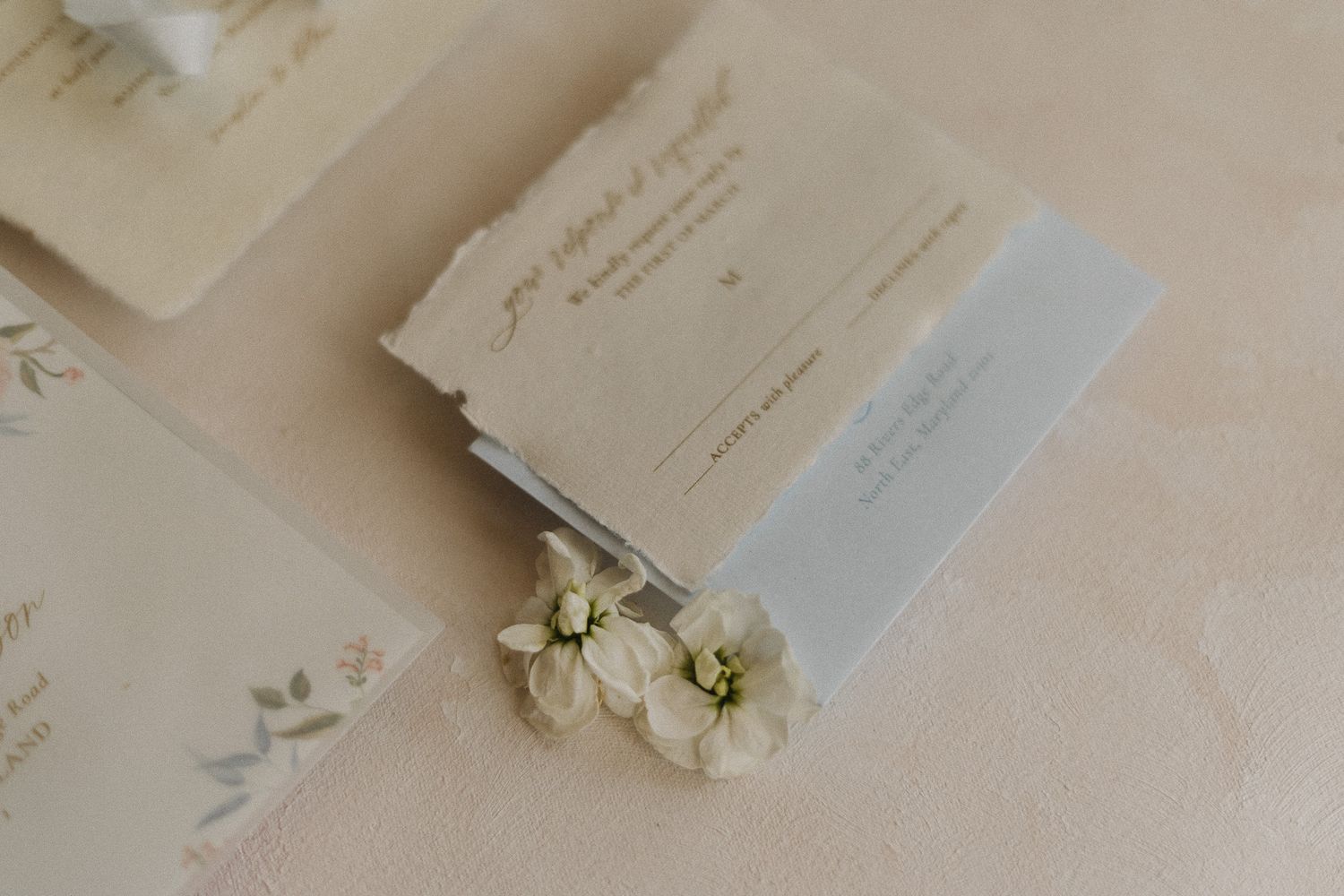 White floral decorations and elegant wedding stationery arranged on a light beige table surface.
