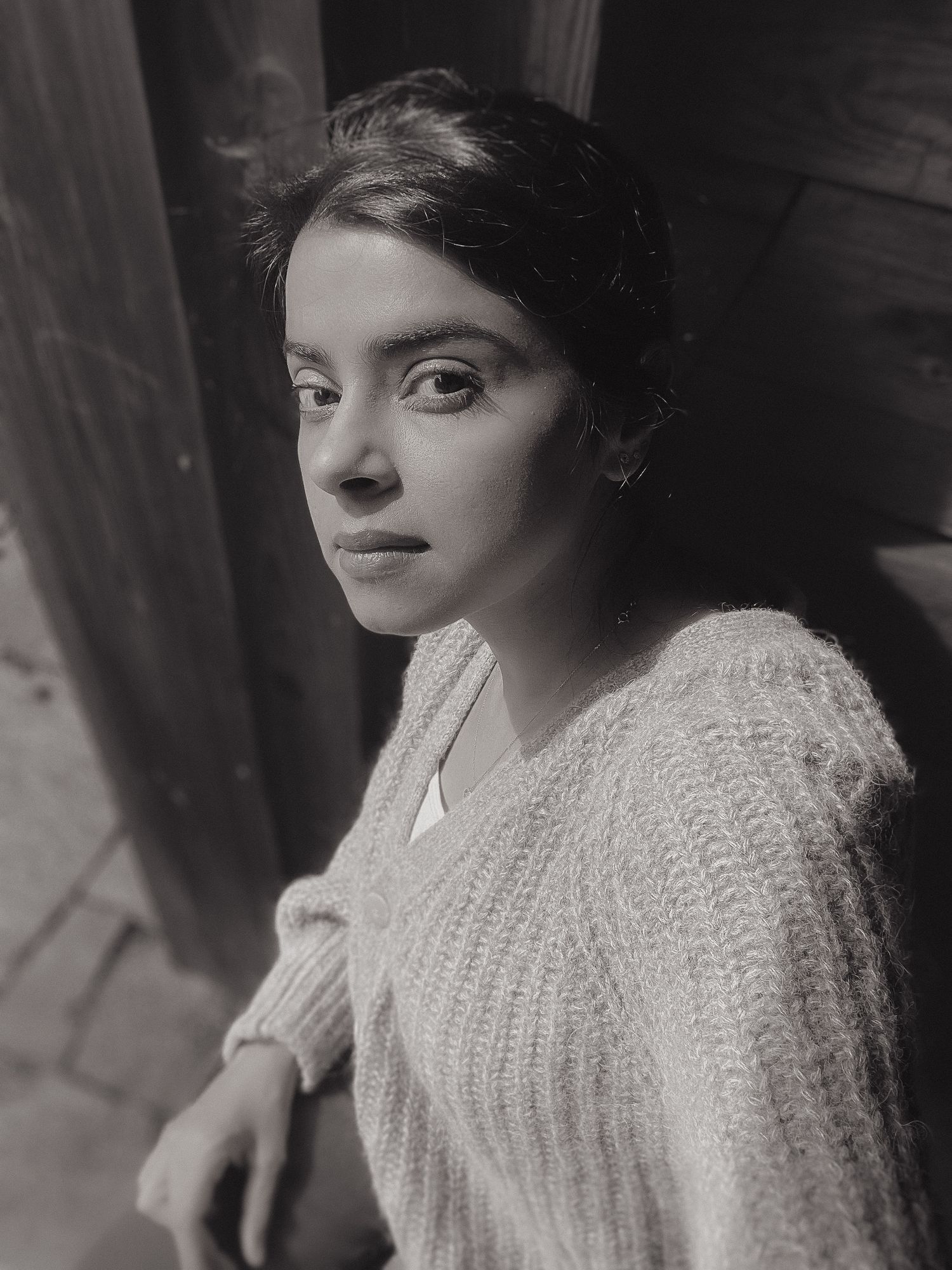 Vintage-style monochrome portrait showing person in cable knit sweater near wooden frame.