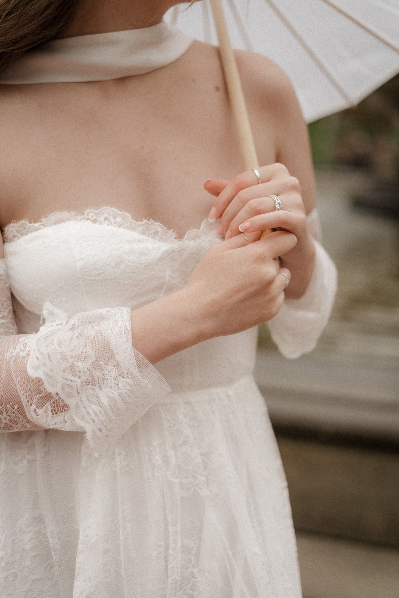 Close-up of a bride’s lace gown and delicate rings, holding a white parasol at Bethesda Terrace in Central Park.