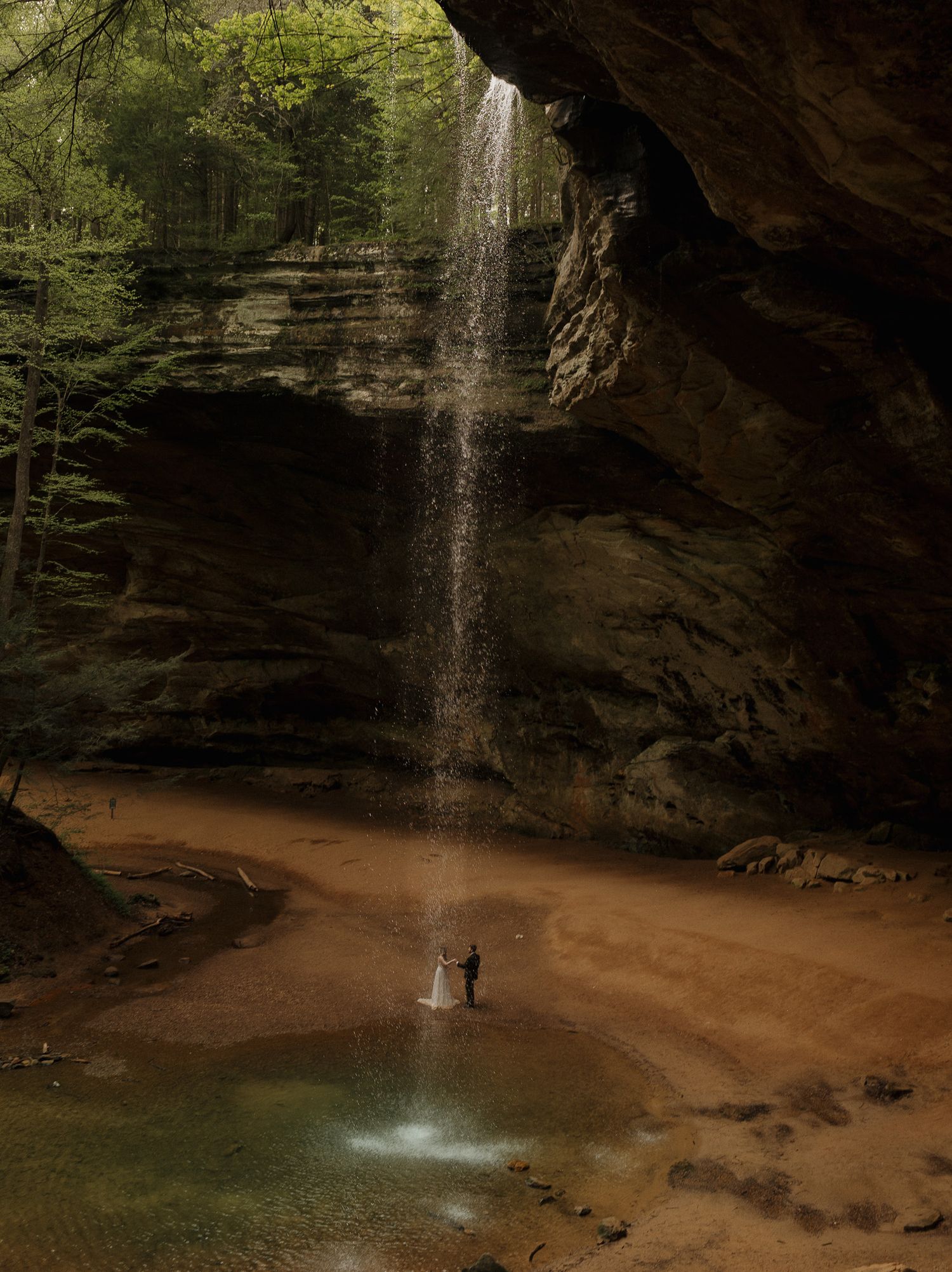 Bride and groom standing beneath a waterfall in a secluded canyon during their adventurous destination elopement.