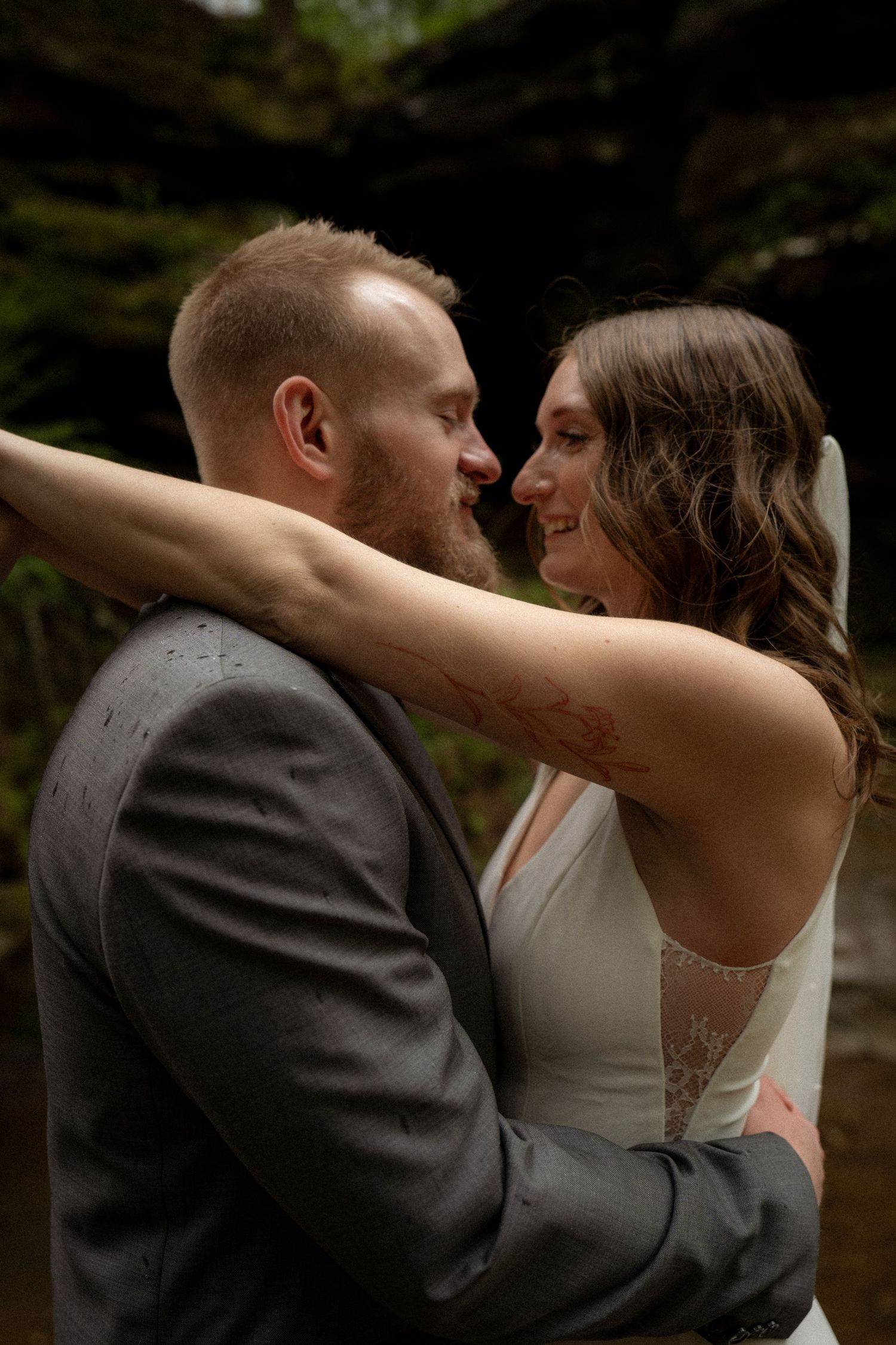Newlyweds embracing among mossy rocks and forest greenery—an intimate moment from their national park destination elopement.