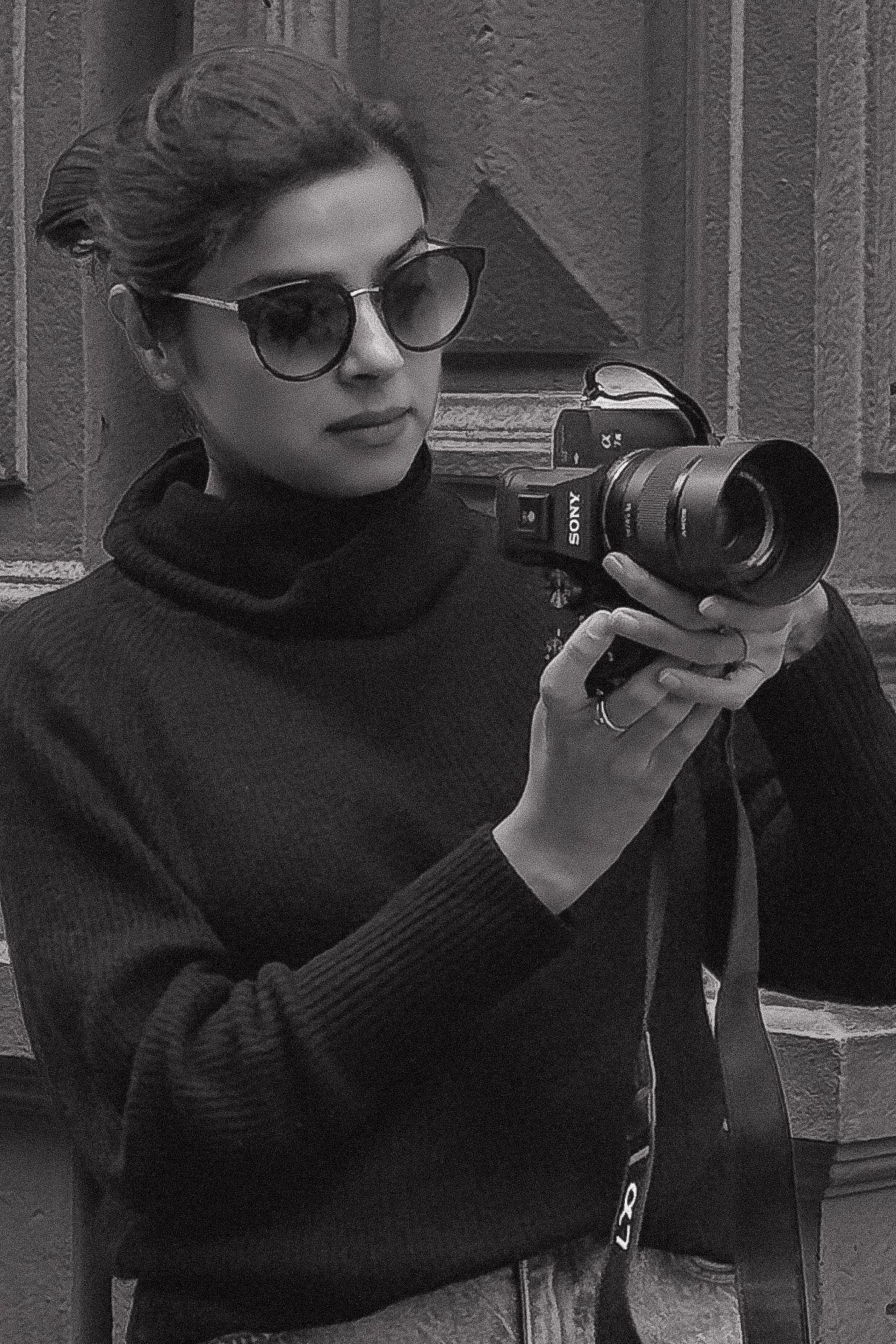 Photographer in dark turtleneck and sunglasses shooting with professional camera in monochrome.