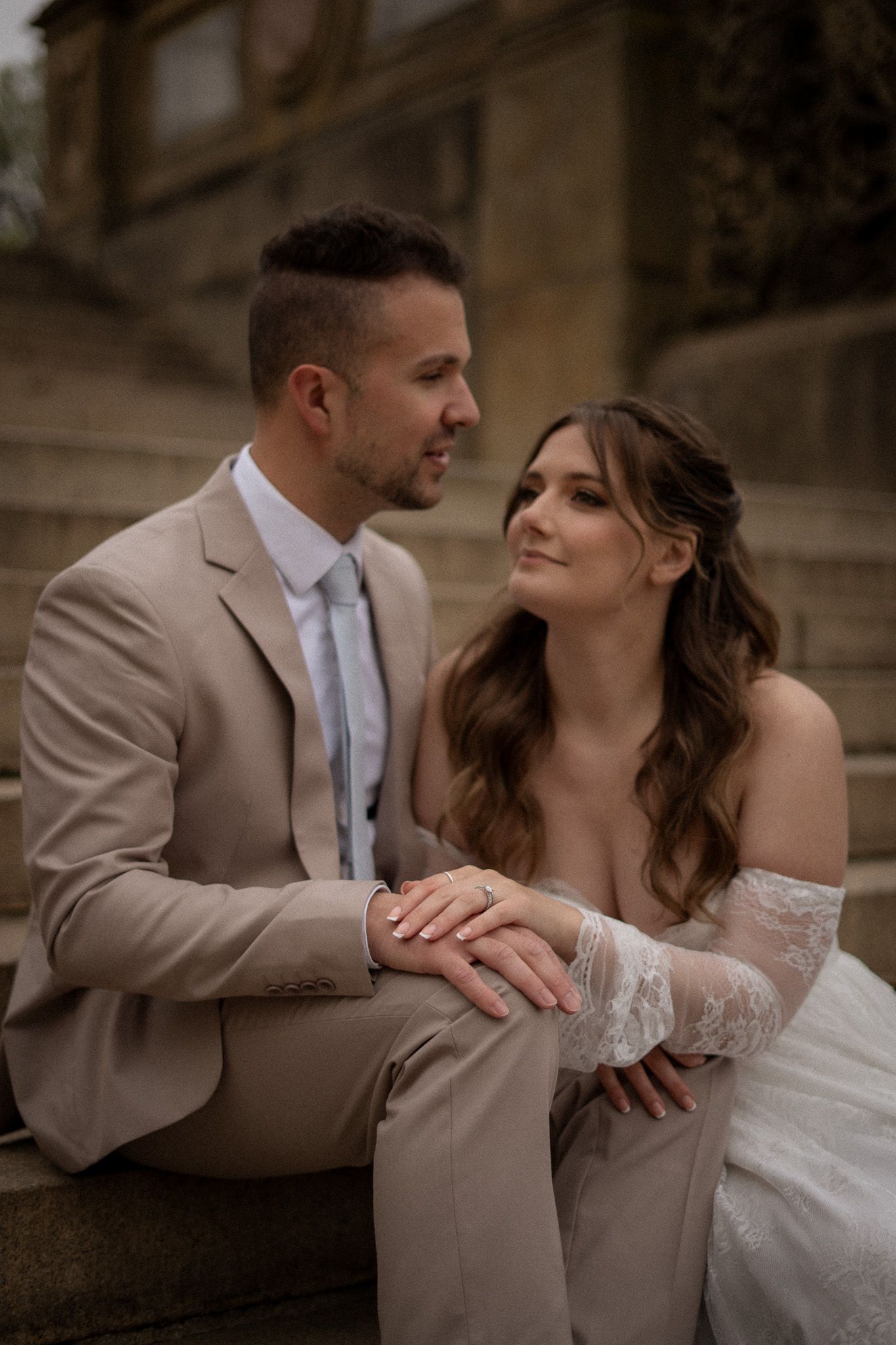 Bride and groom sitting on stone steps, holding hands and sharing an intimate moment at Bethesda Terrace, Central Park.