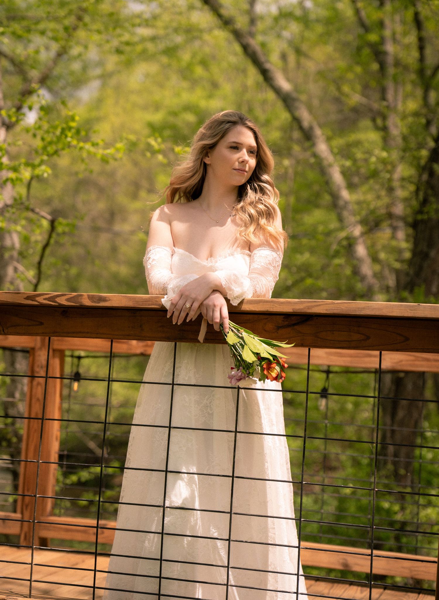 Bride leaning on a wooden bridge railing, lost in thought during her New York elopement in a quiet forest setting.