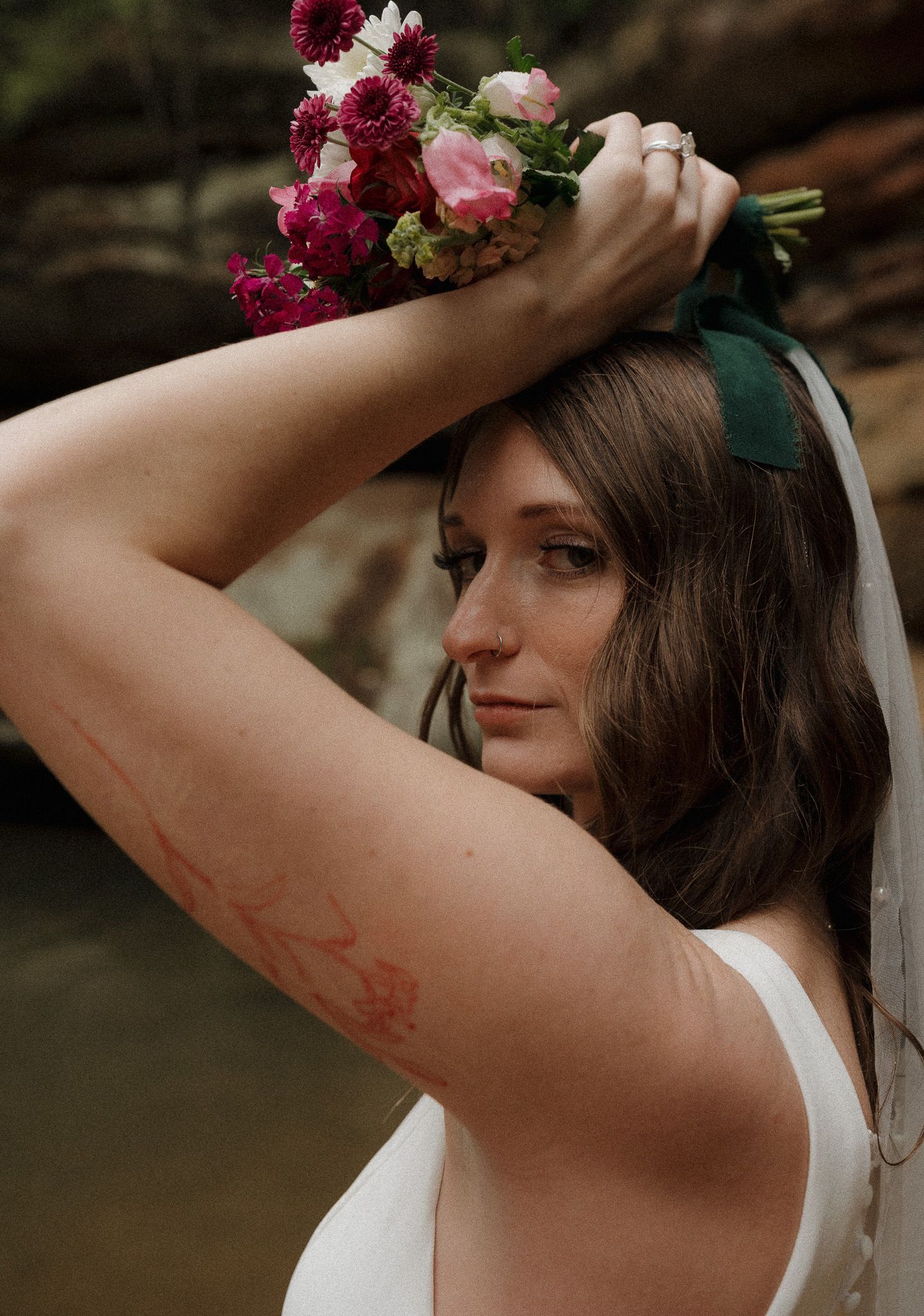 Bride holding a vibrant bouquet over her head, looking into the camera with soft confidence