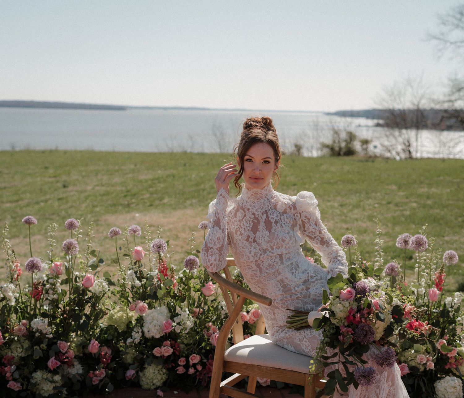 A dreamy outdoor scene with a wooden chair surrounded by pink roses and wildflowers against a lakeside backdrop.