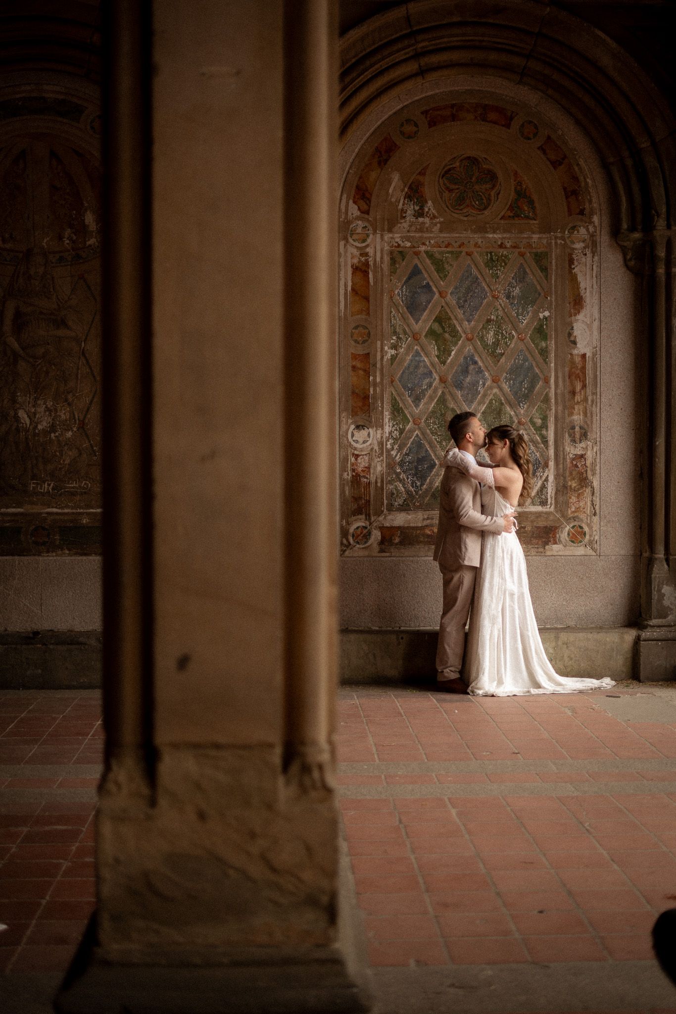 Bride and groom embracing under the ornate arches of Bethesda Terrace, Central Park, NYC.