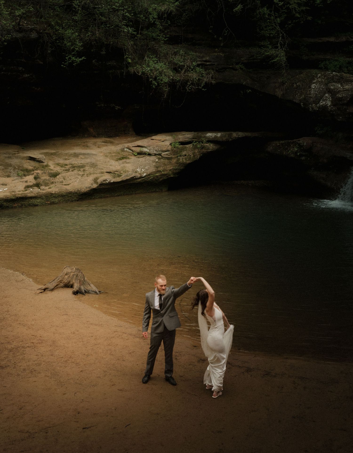 New York couple celebrating with a twirl by the water’s edge, surrounded by forest and soft light.