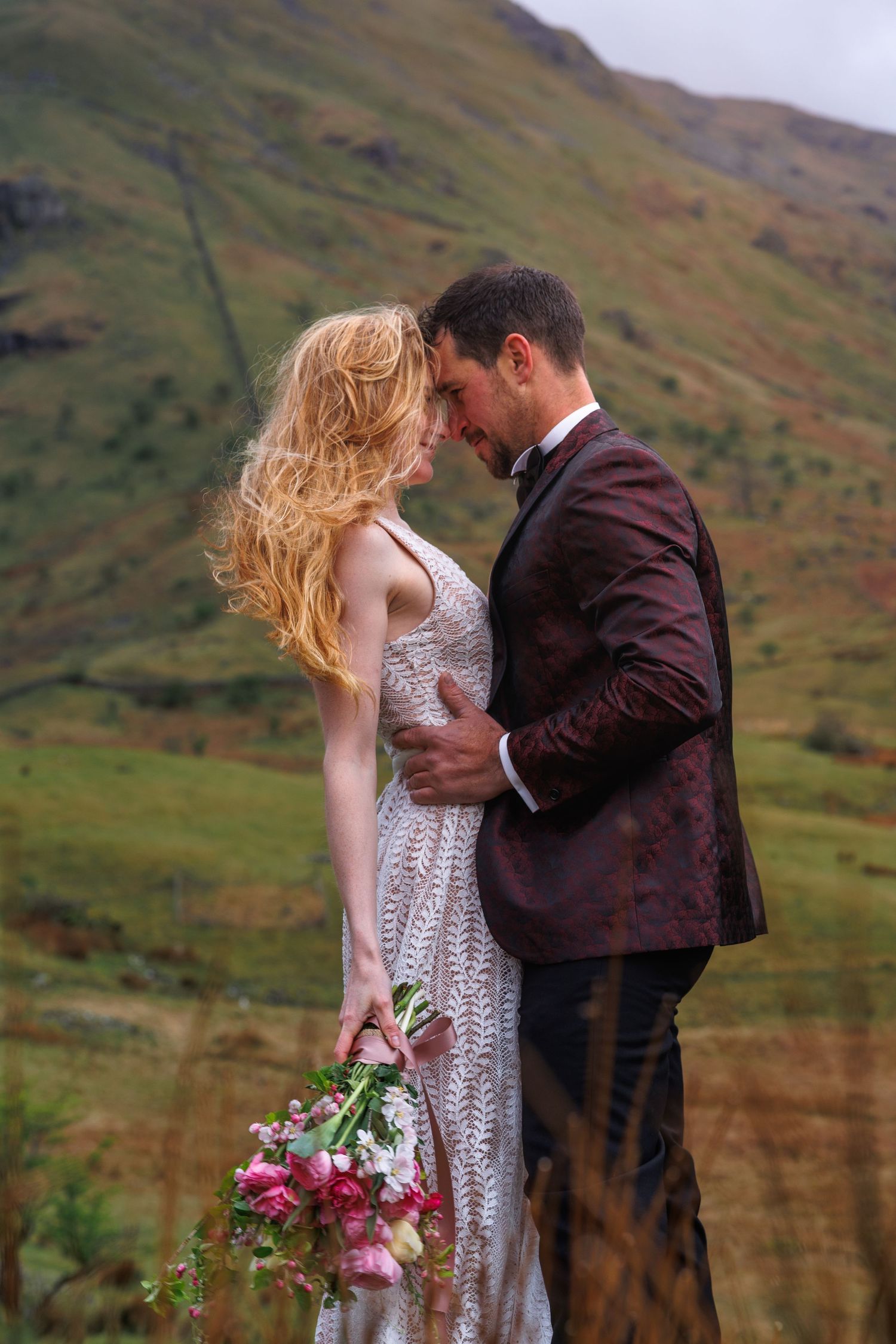 A romantic moment against dramatic mountain scenery with figure holding pink flowers.