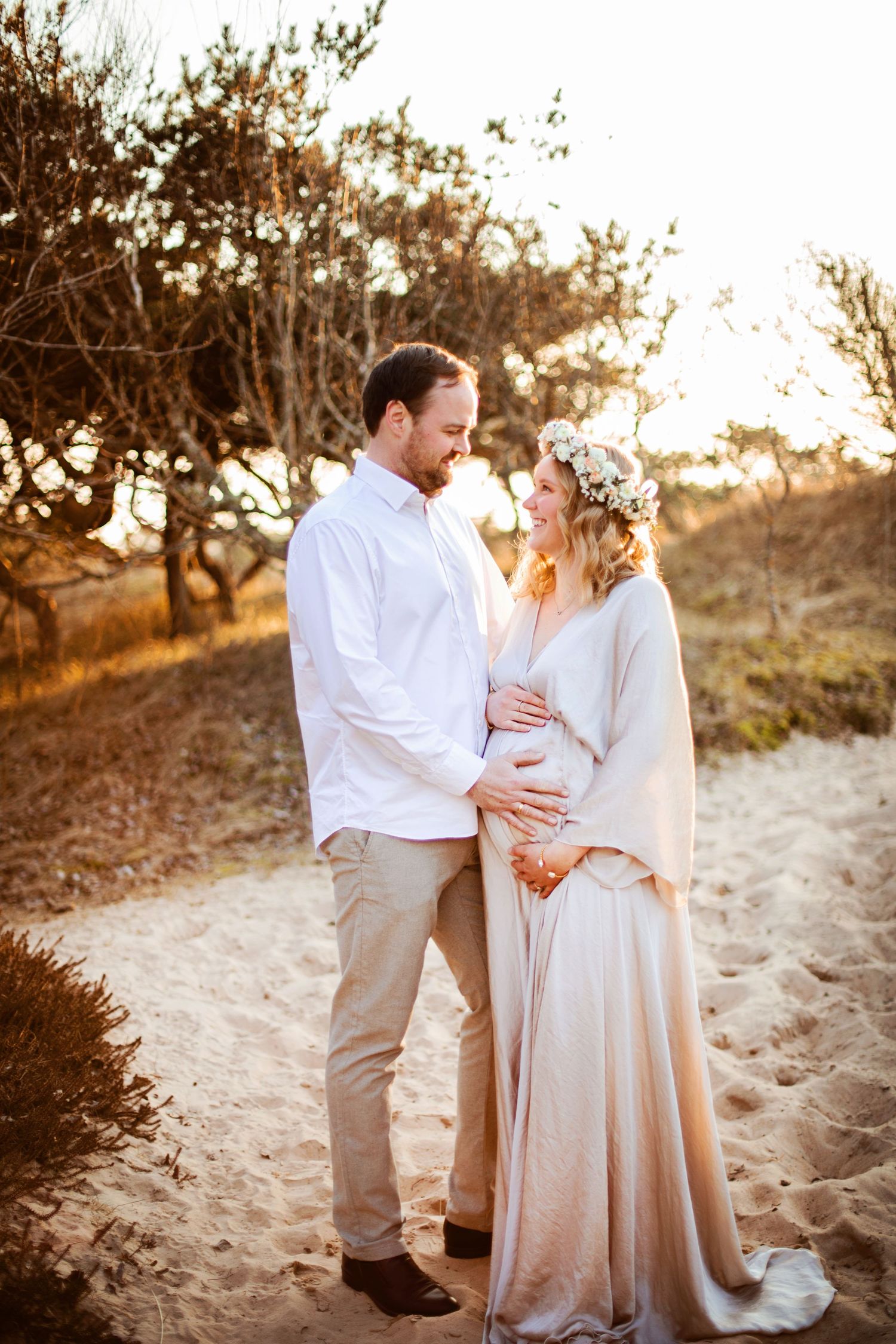 A couple shares a tender moment on a sandy beach path during golden hour sunset.
