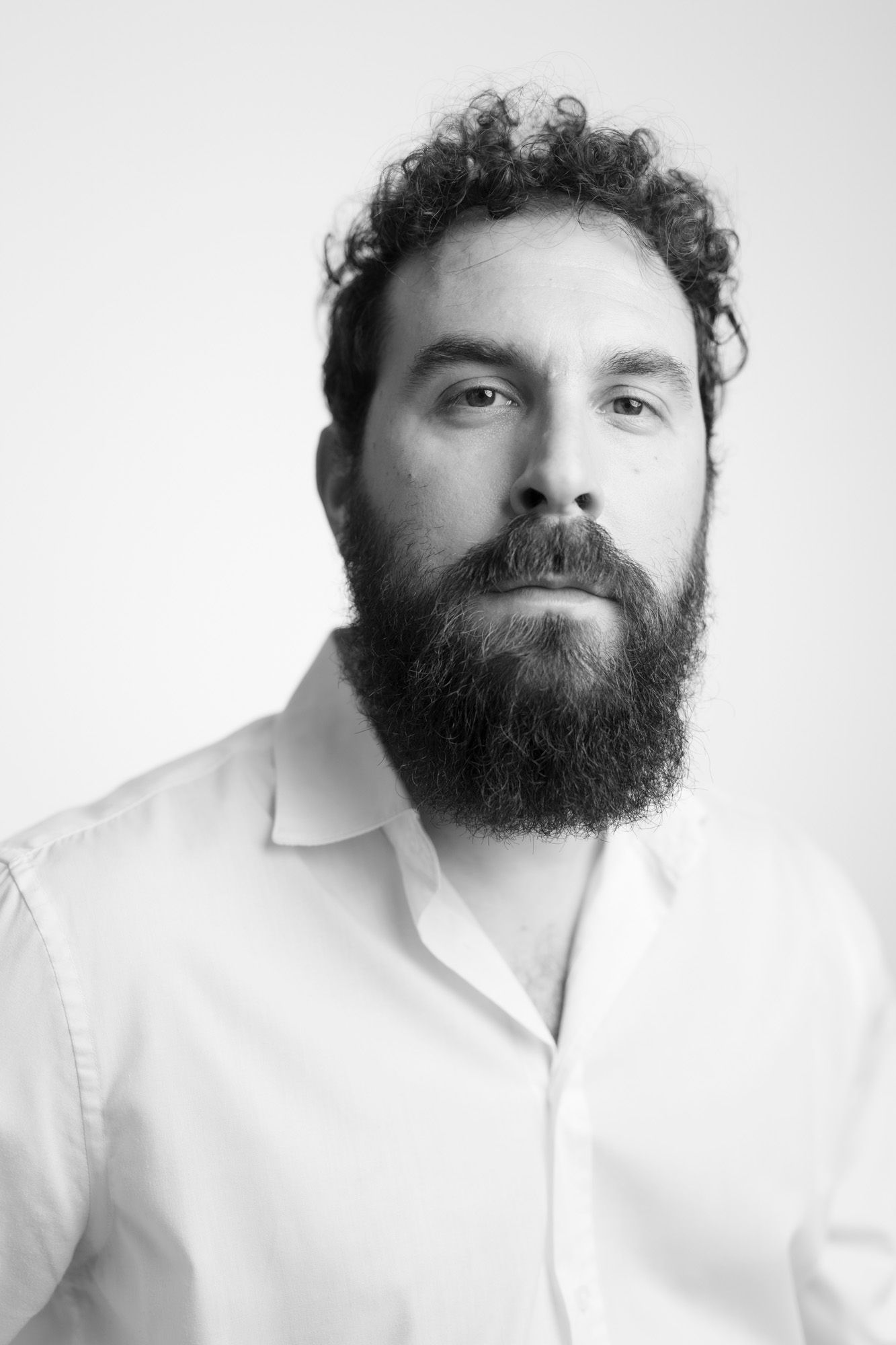 Black and white portrait of a person wearing a white shirt with curly hair and a full dark beard.