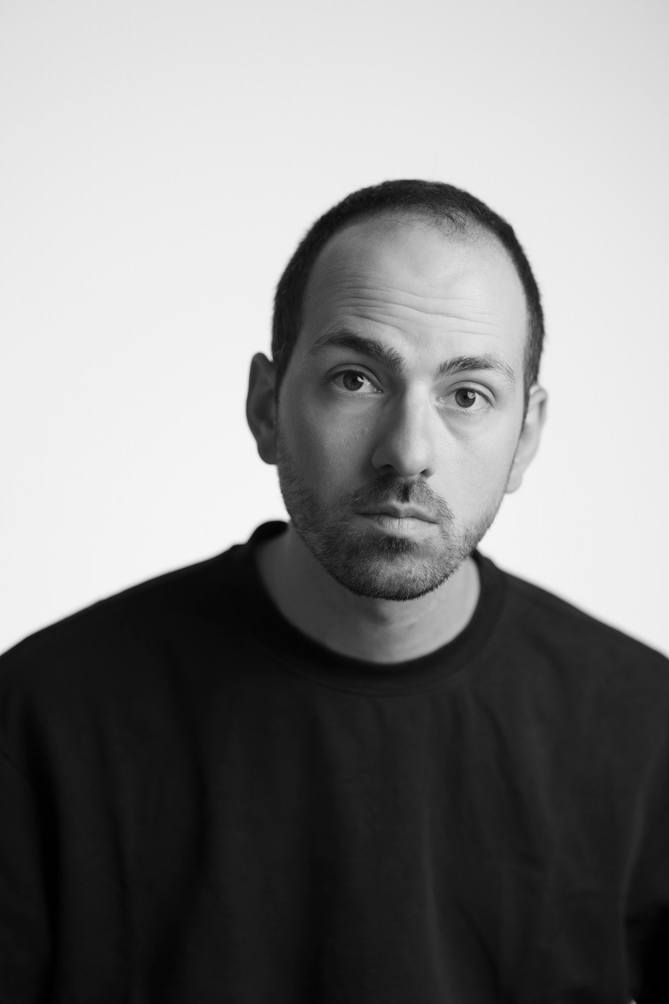 Black and white portrait photograph of a person wearing a dark sweatshirt against a light background.