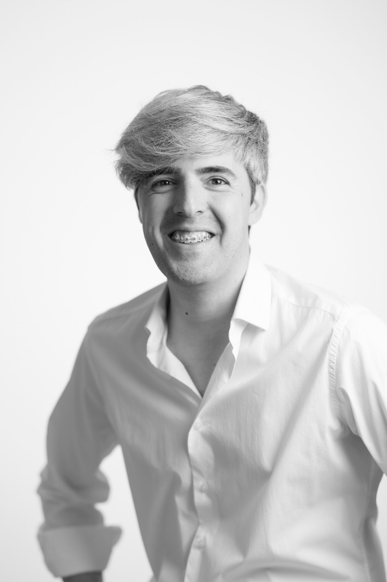 Black and white portrait photo of a young person with styled hair wearing a white button-down shirt against a light backdrop.