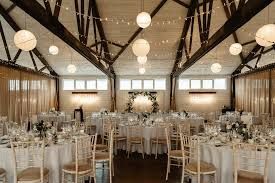 Elegant wedding reception venue with white paper lanterns, exposed wooden beams, and tables set for dining celebrations.