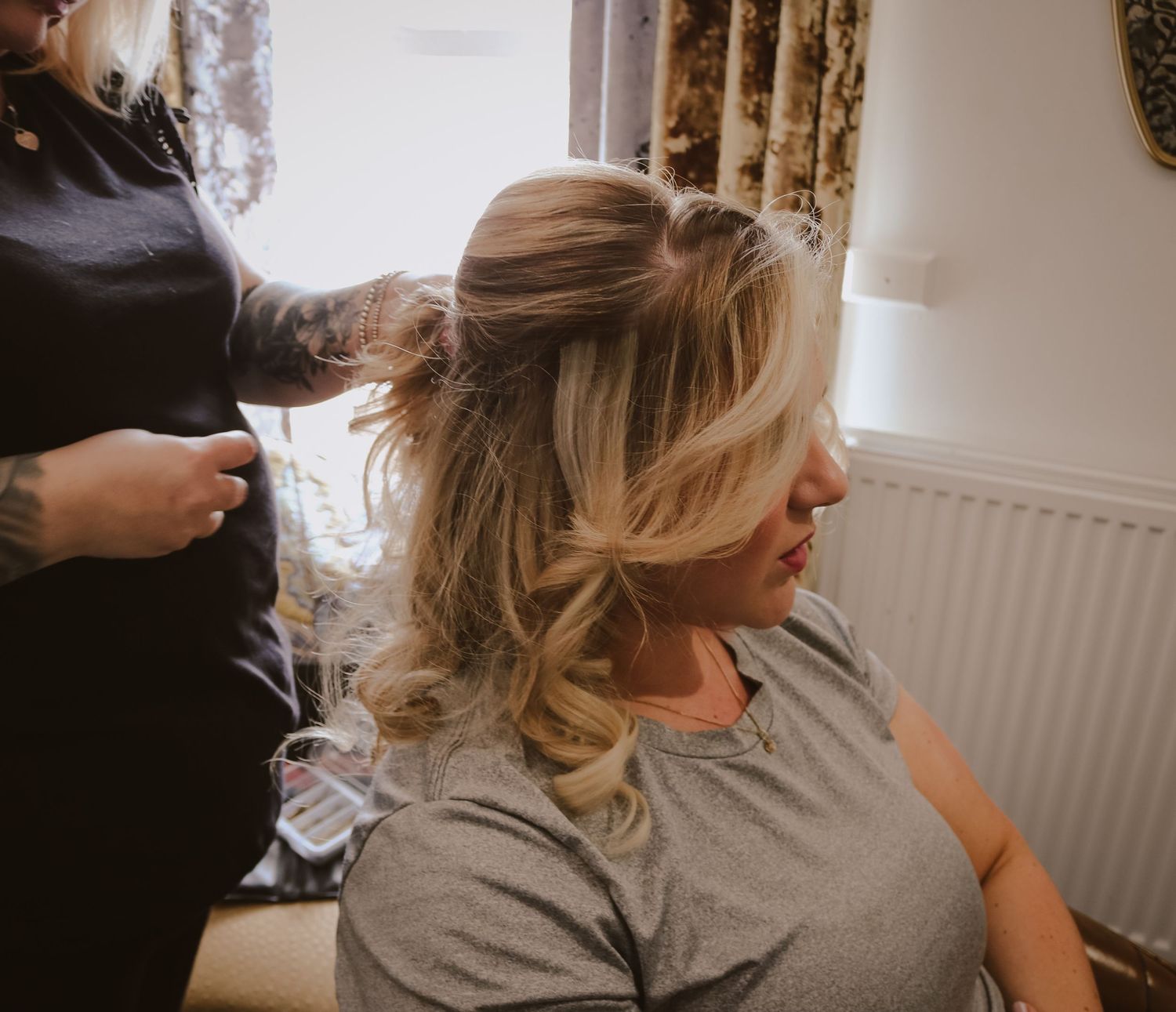 A hairstylist styles blonde wavy hair in an elegant updo at a salon appointment.