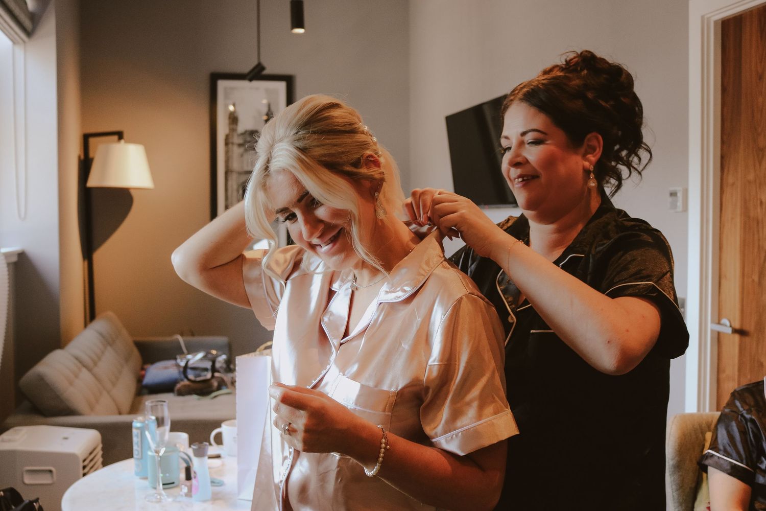 Wedding preparation scene with stylists helping arrange details in warm, natural lighting.