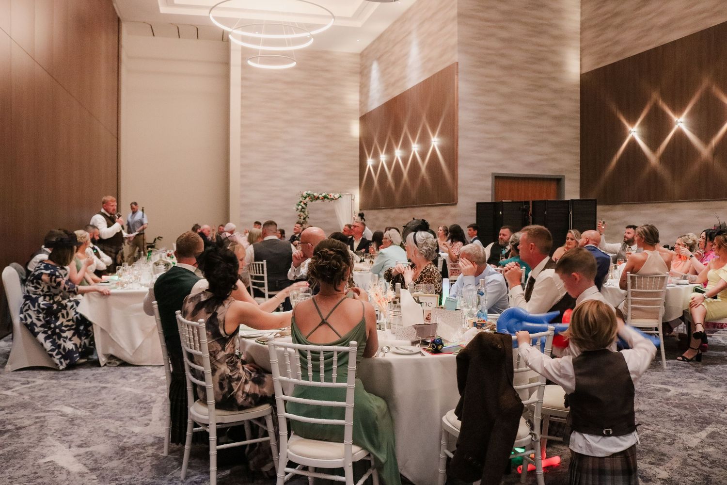 Wedding reception dinner at an elegant modern venue with white tables and geometric wall lighting decorations.