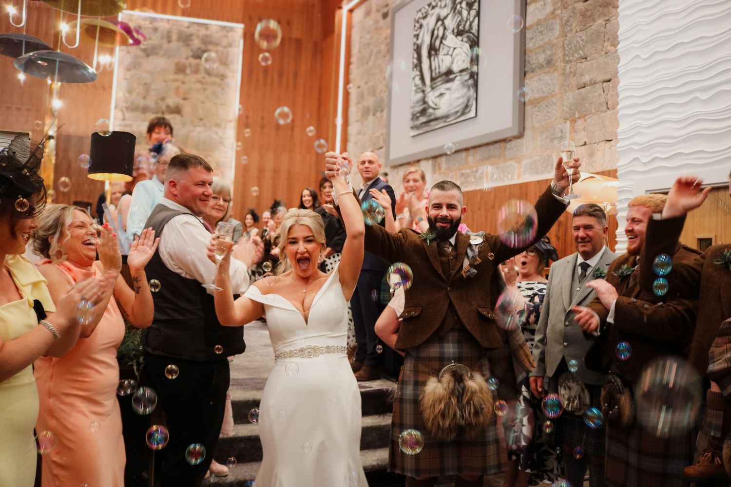 Wedding celebration at a rustic venue with exposed brick walls as guests joyfully gather while bubbles float through the air.