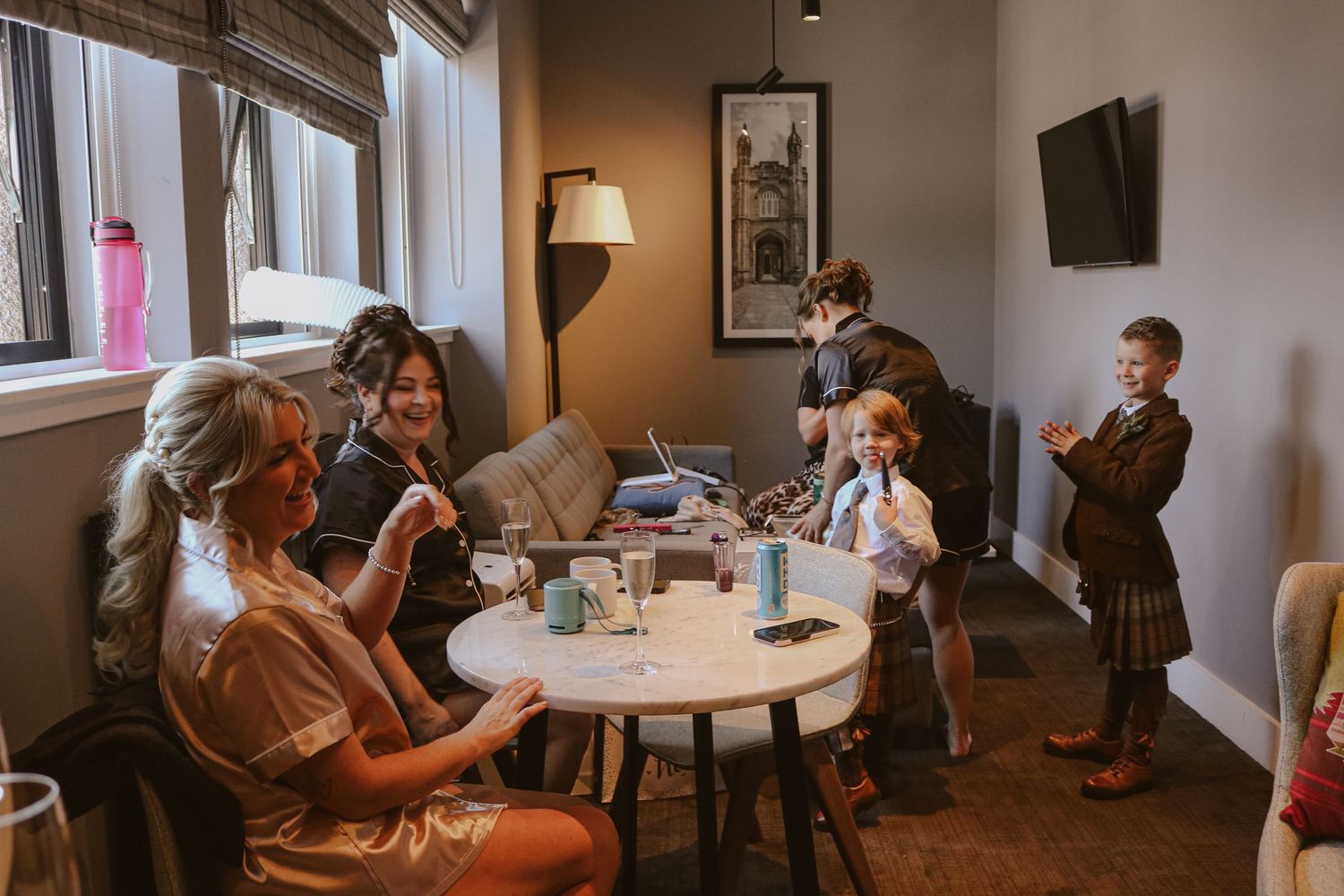 A group gathers around a white round table in a cozy cafe corner with warm lighting and curtained windows.