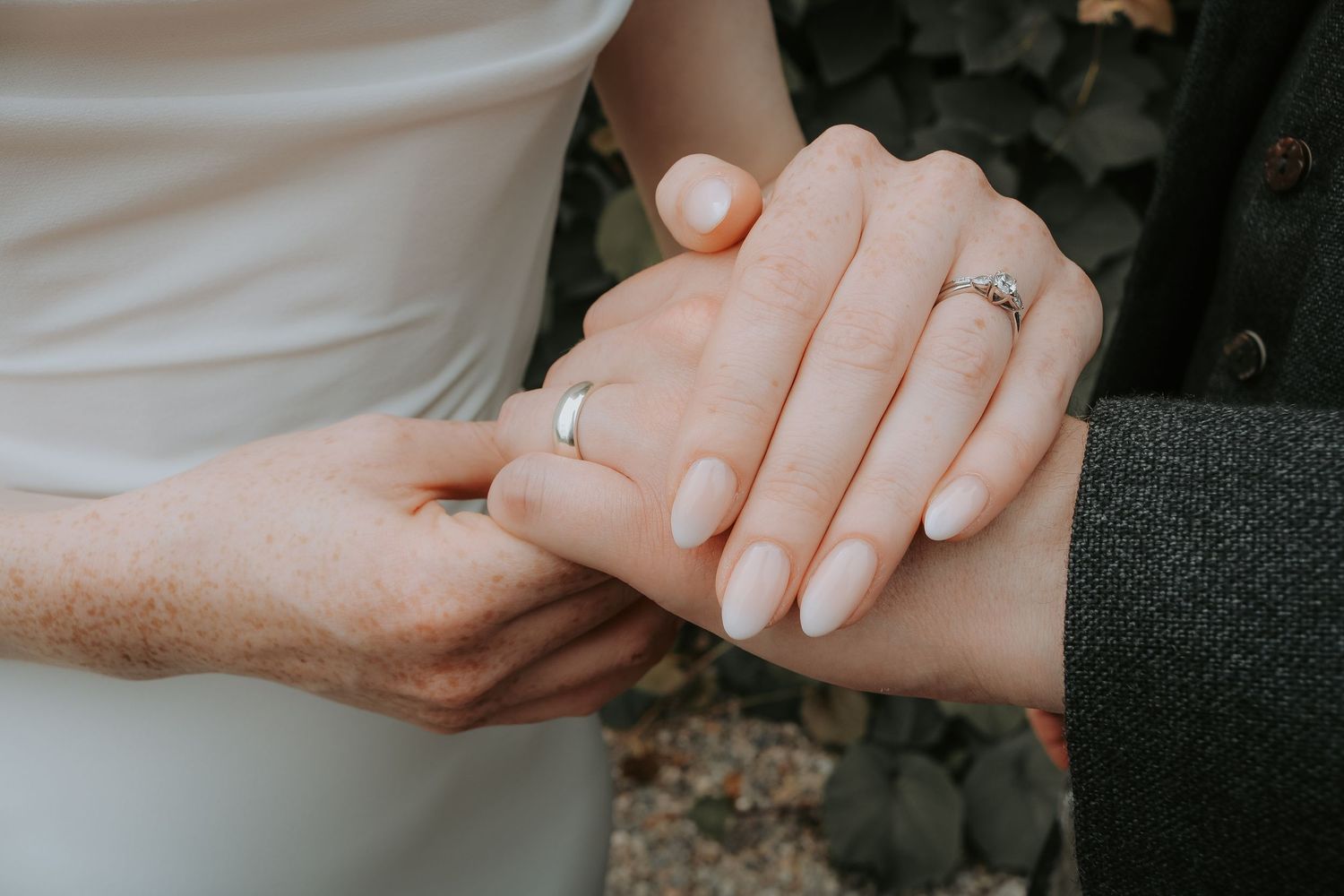 Close up of hands clasped together showing an engagement ring with white nail polish on the nails.