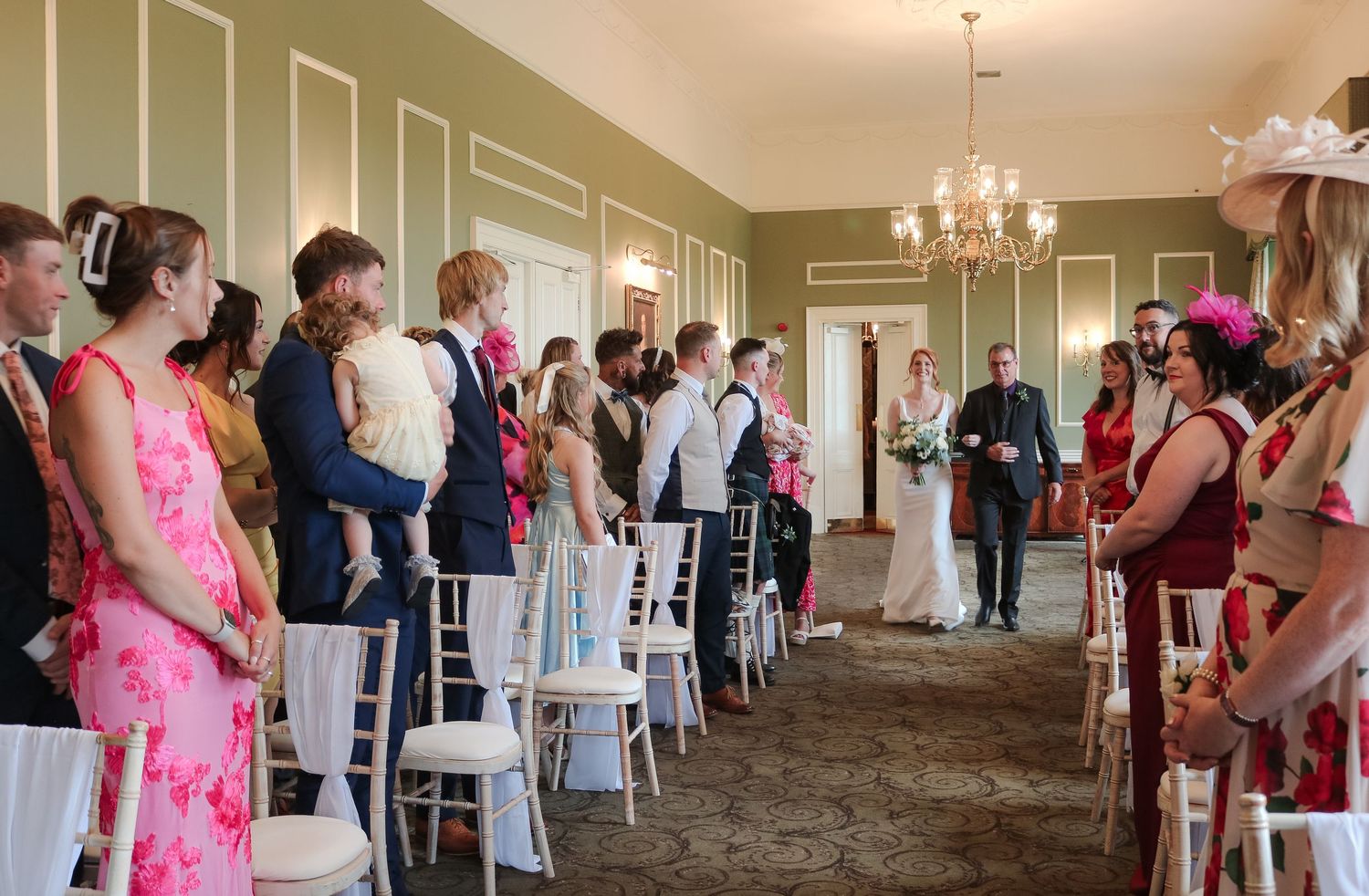 A panoramic view of people standing in an elegant reception hall with green walls and crystal chandeliers.